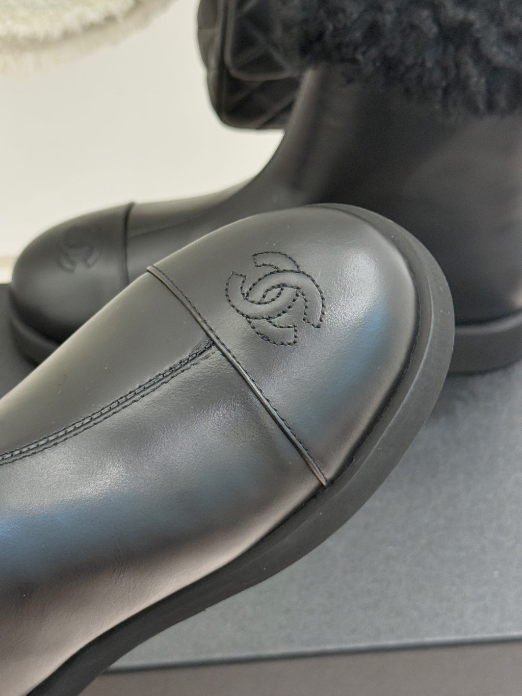 Close-up of black leather ankle boot with embossed logo and curved stitch line