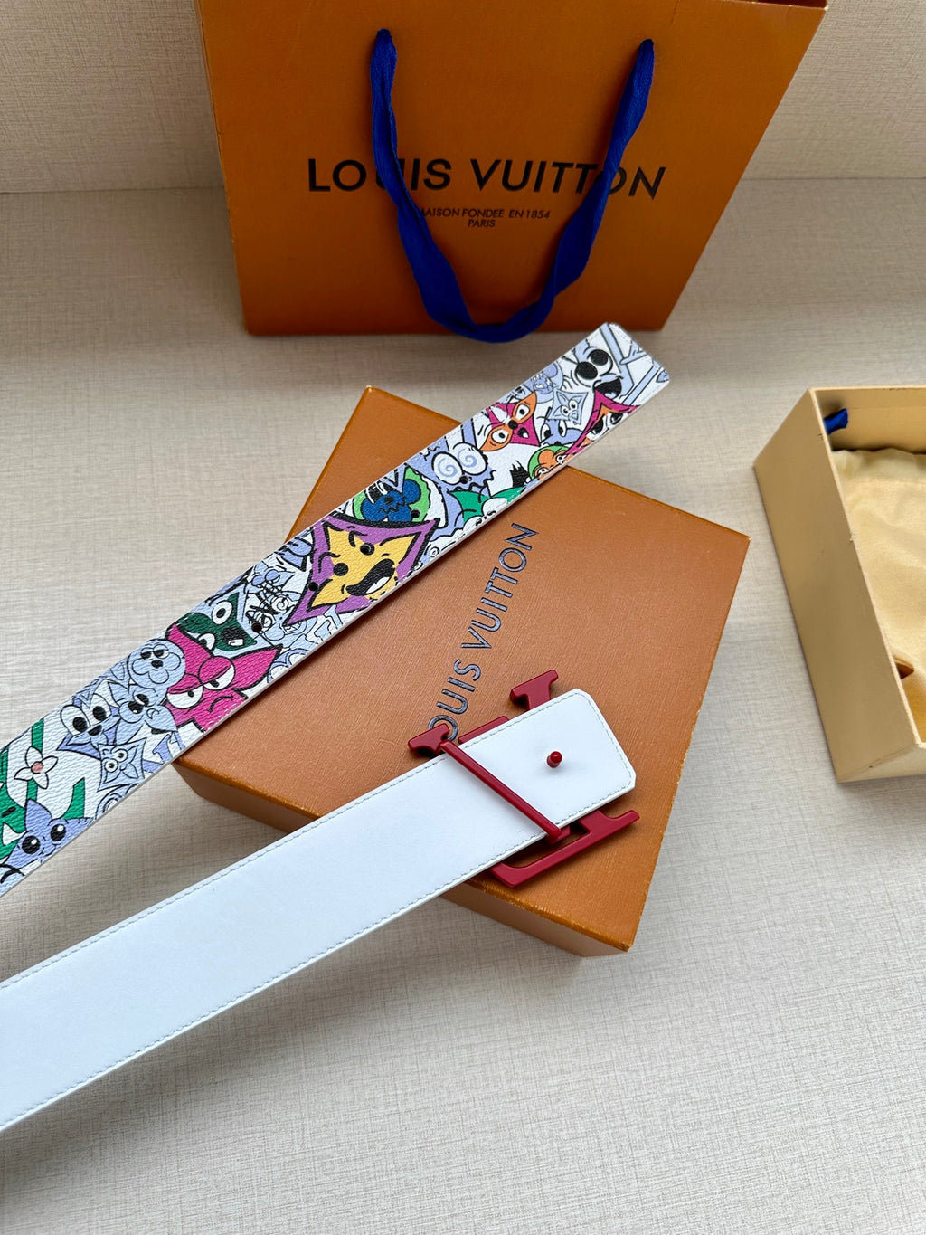 Printed belt with white strap, red LV buckle, and multicolor character motif