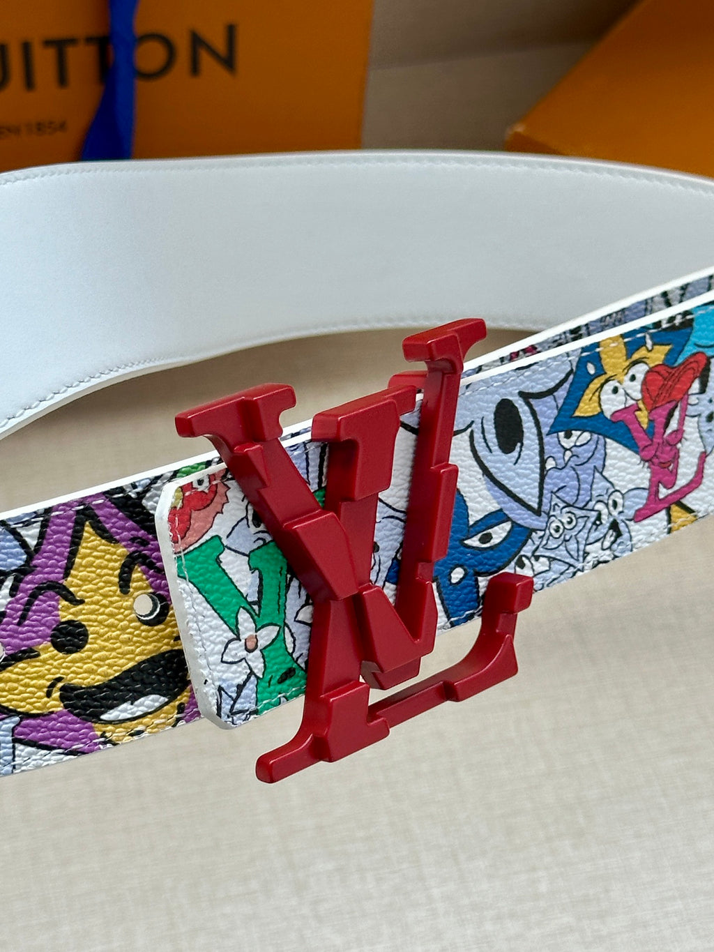 White printed belt with red LV buckle, graphic strap close-up