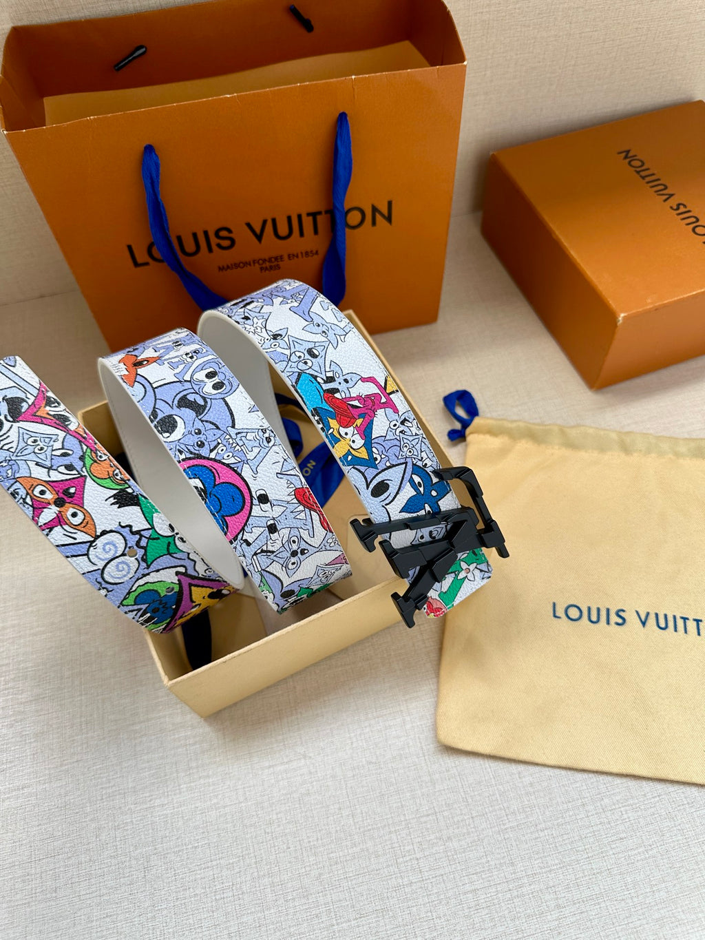 Louis Vuitton belt, white multicolor graphic strap with black LV buckle, angled view