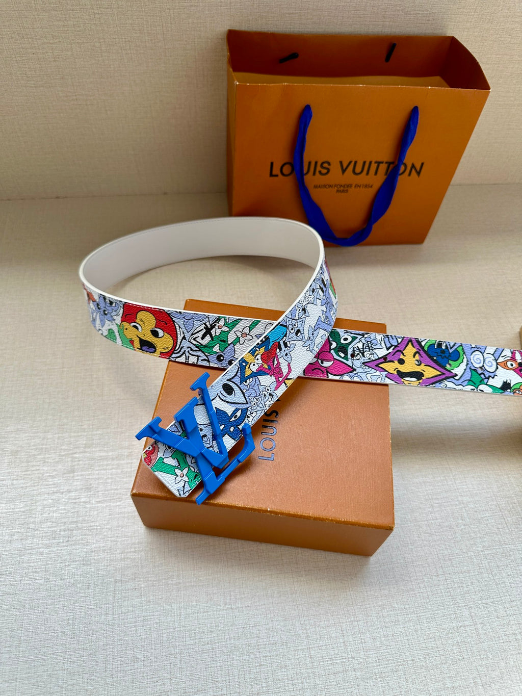 Louis Vuitton belt laid flat: white comic print strap with blue LV buckle