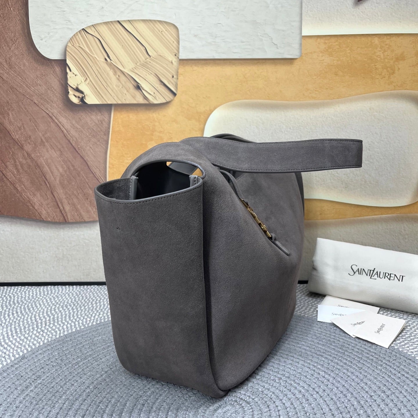 Dark gray suede tote bag shown from side with top handles and gold zipper detail
