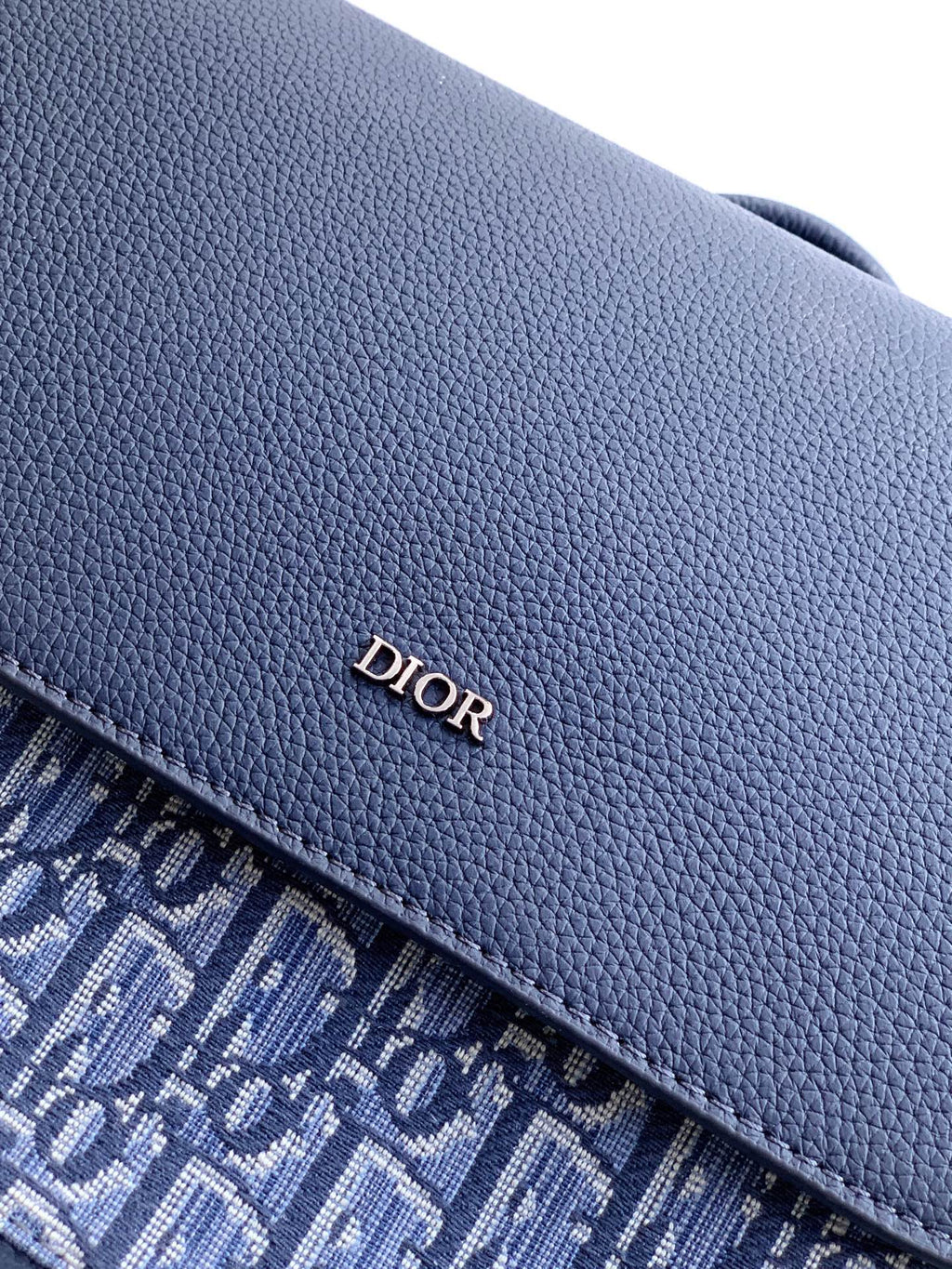 Navy Dior backpack bag close-up of pebbled leather flap with Dior logo stitching.