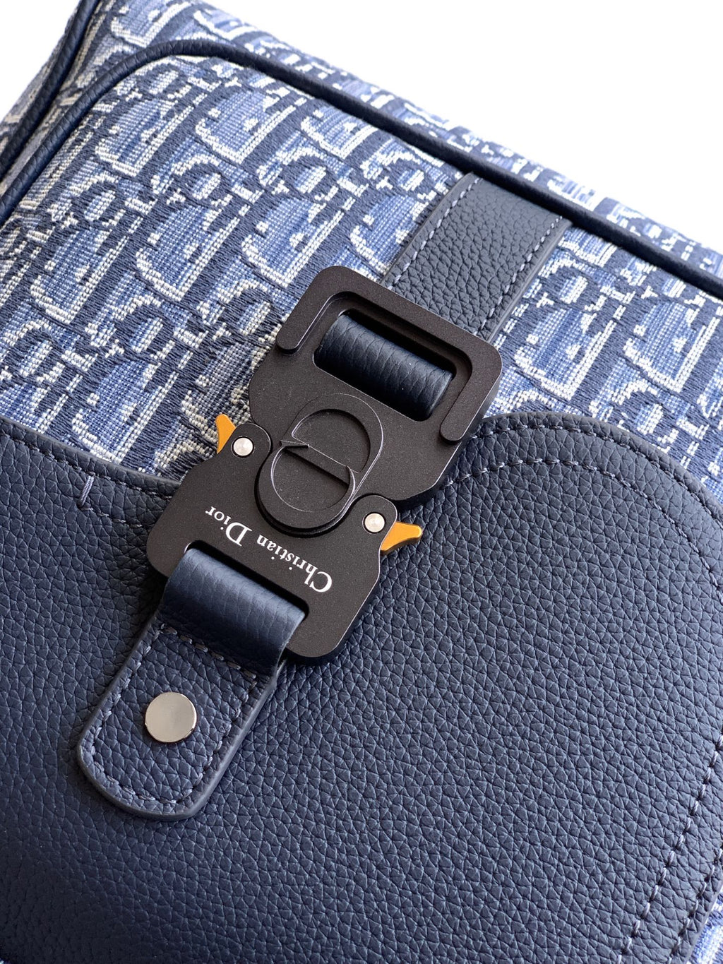 Dior backpack front clasp hardware on textured leather and logo canvas.