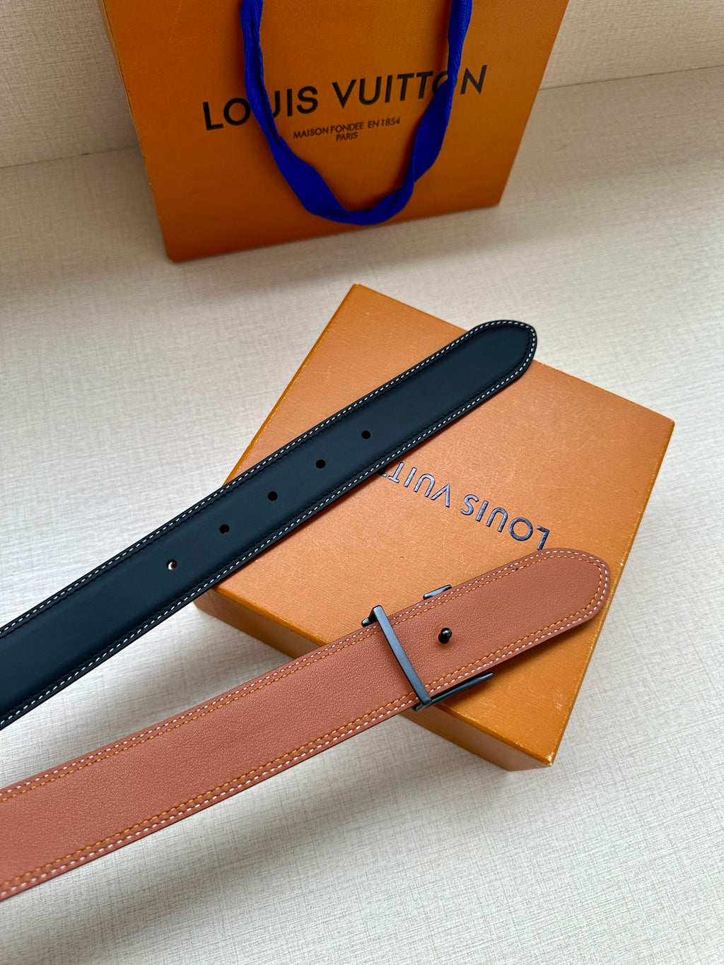 Louis Vuitton leather belt with dark blue strap, tan underside, and metal buckle.