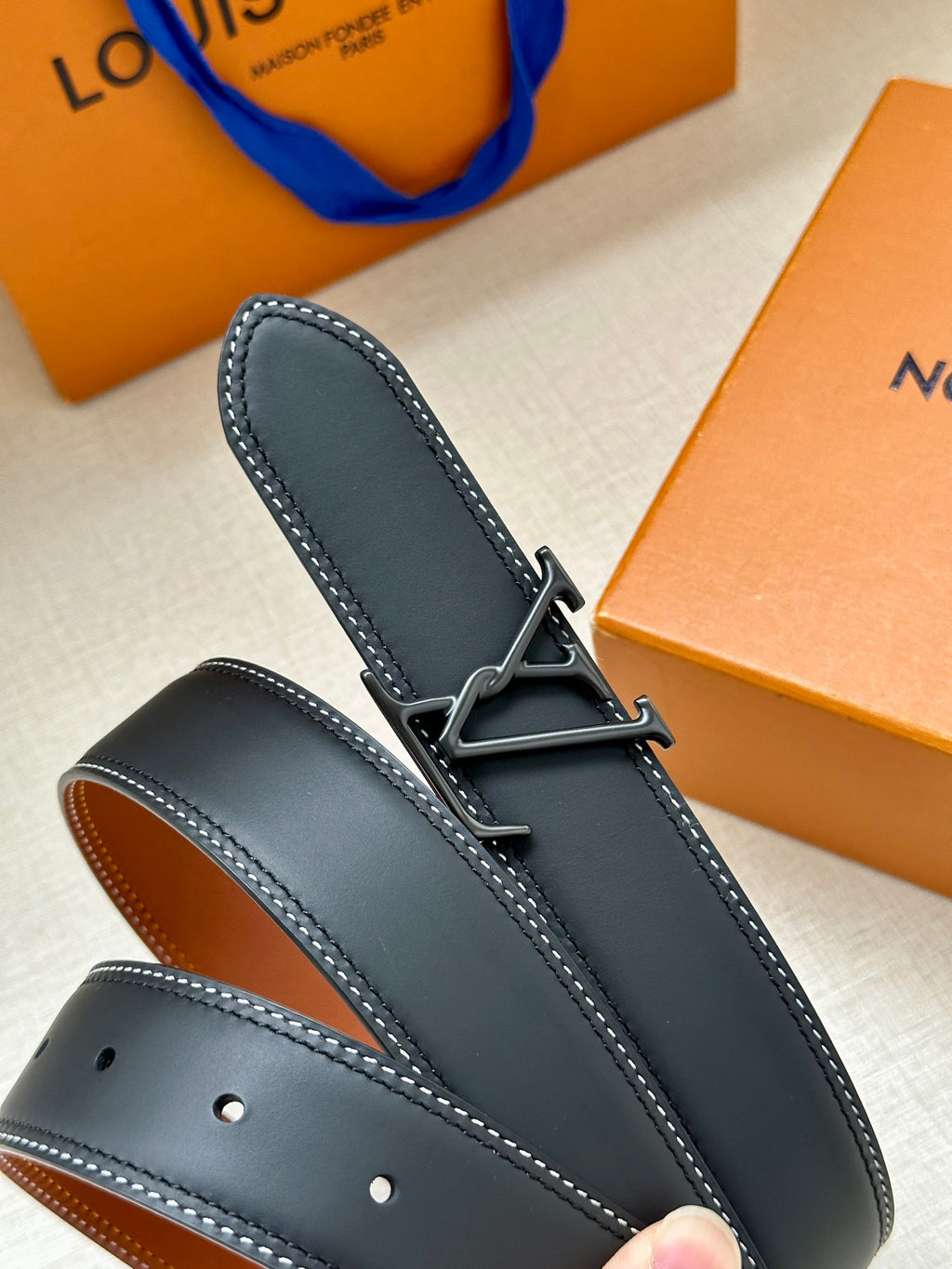 Louis Vuitton belt end with hole row, dark blue leather strap and tan underside.