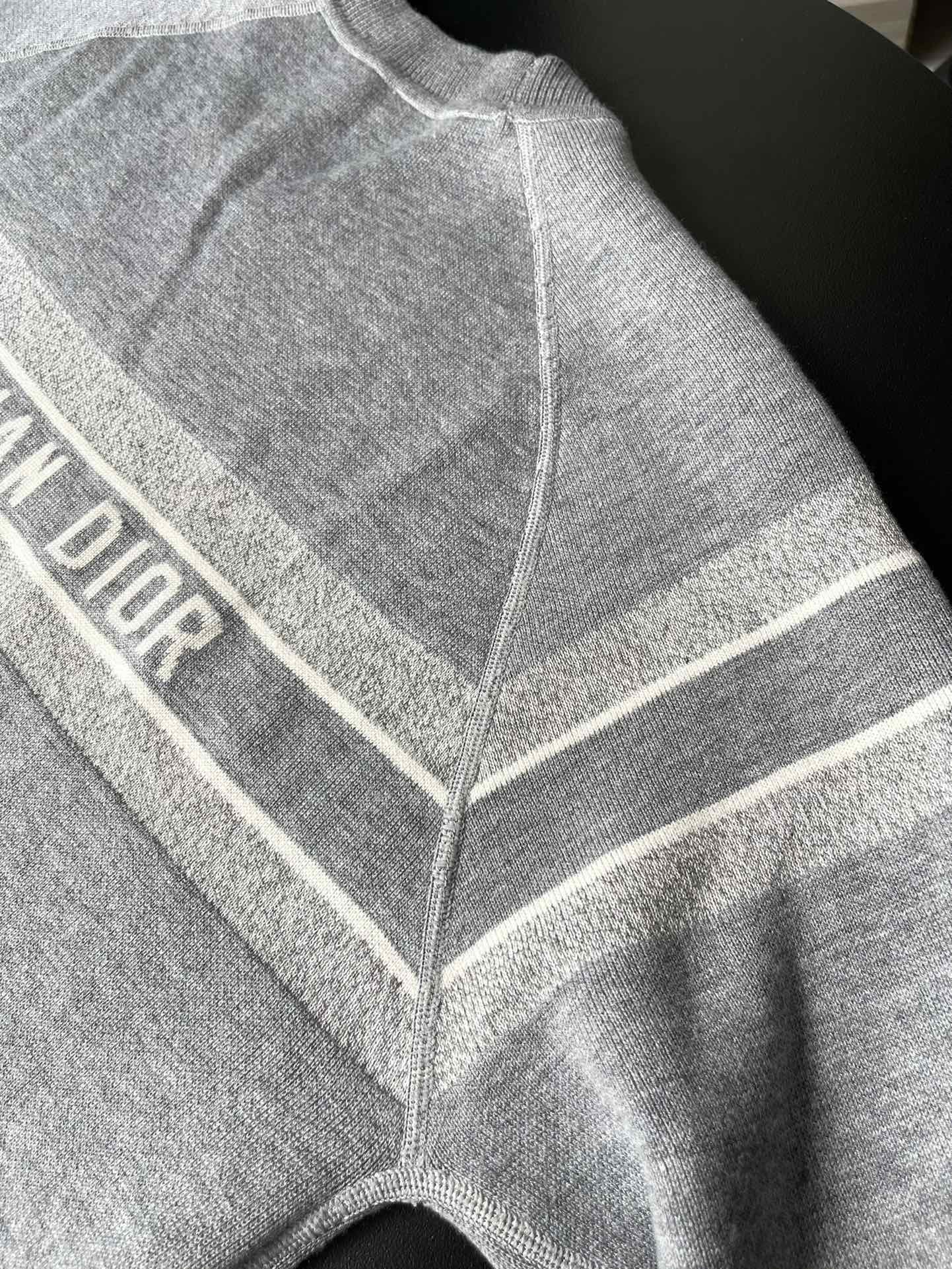 Gray long-sleeve sweater close-up with striped trim and V seam detail