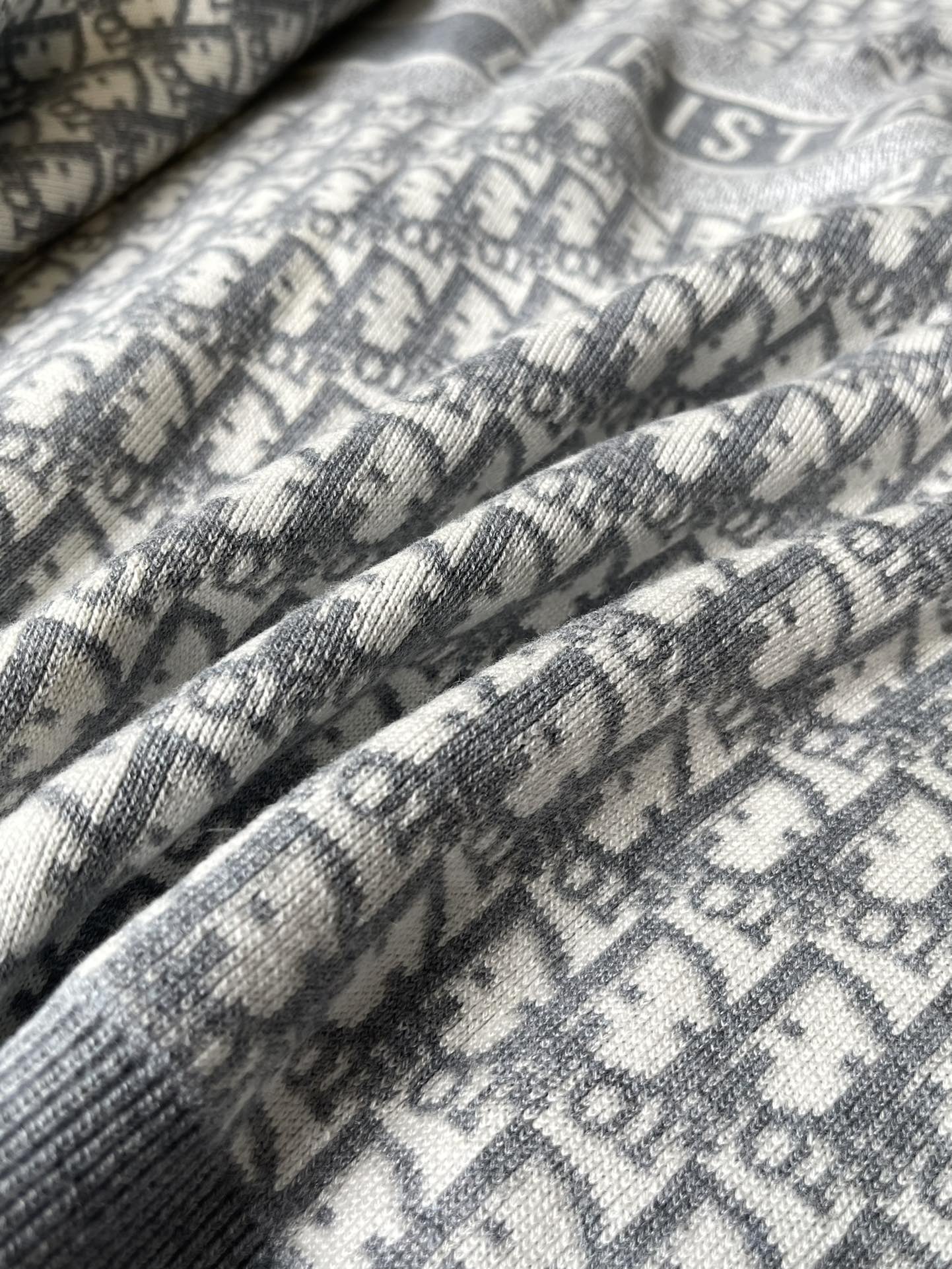 Gray sweater fabric close-up with repeating monogram lettering pattern