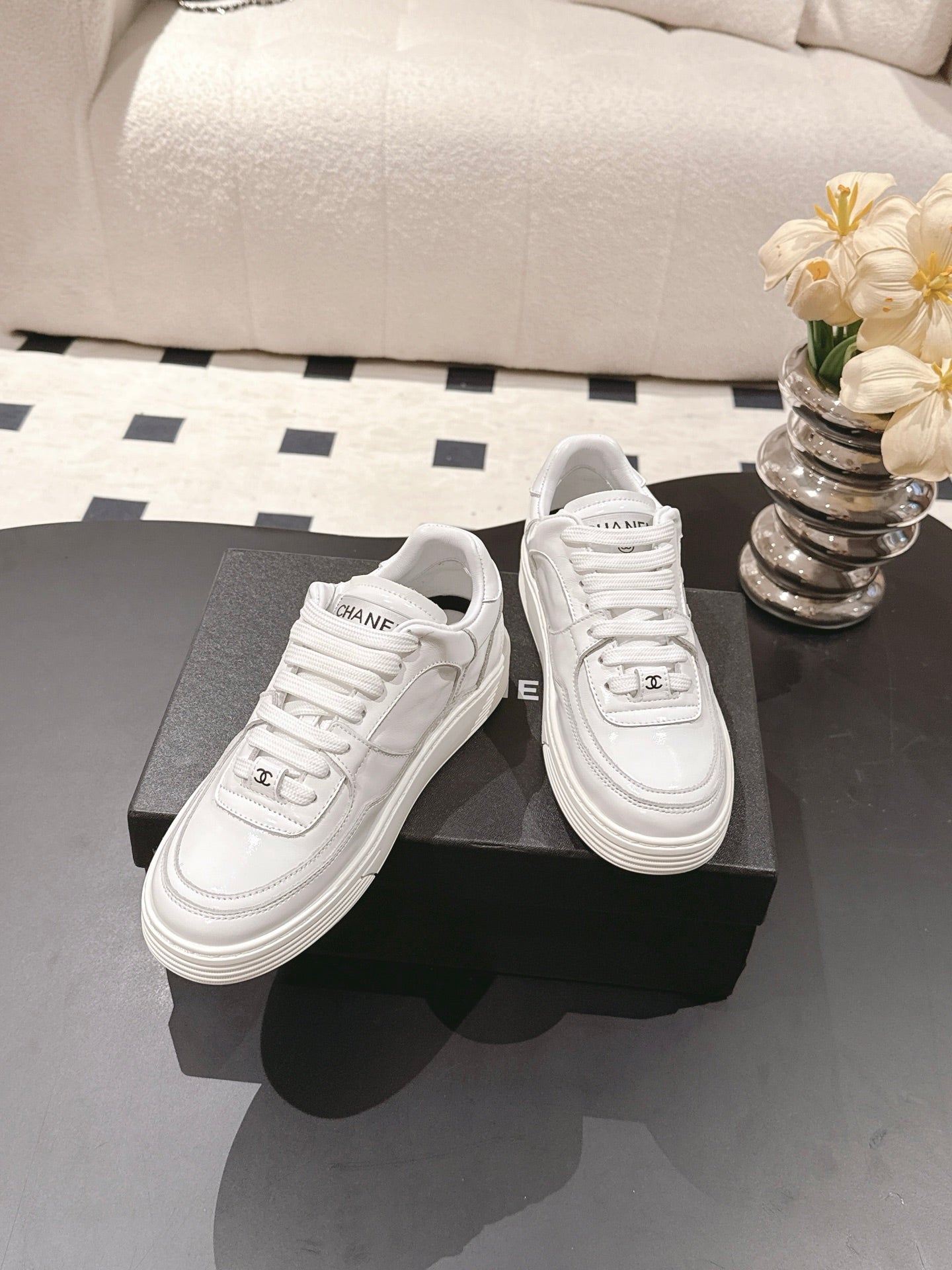 White low-top sneakers at angle, showing toe caps, laces, and side logo stitching