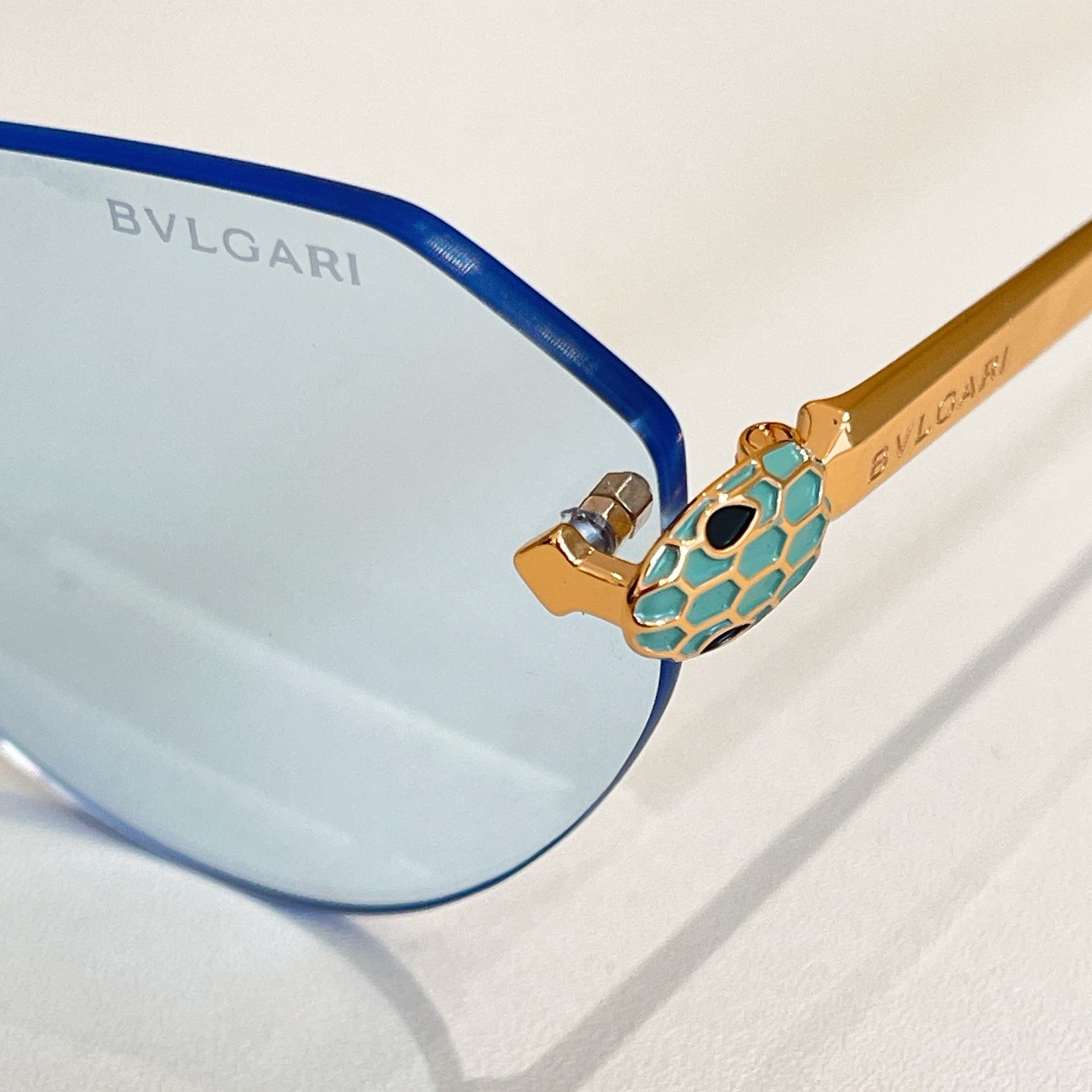 Bvlgari sunglasses close-up with blue lens, blue temples and teal decorative hinge.