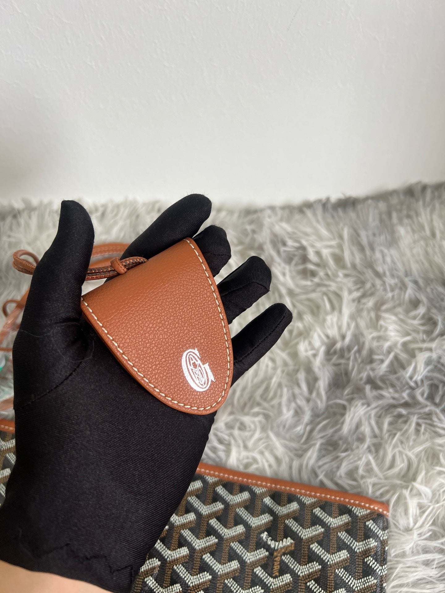 Goyard mini pouch on black gloves, brown leather flap and dark monogram pattern