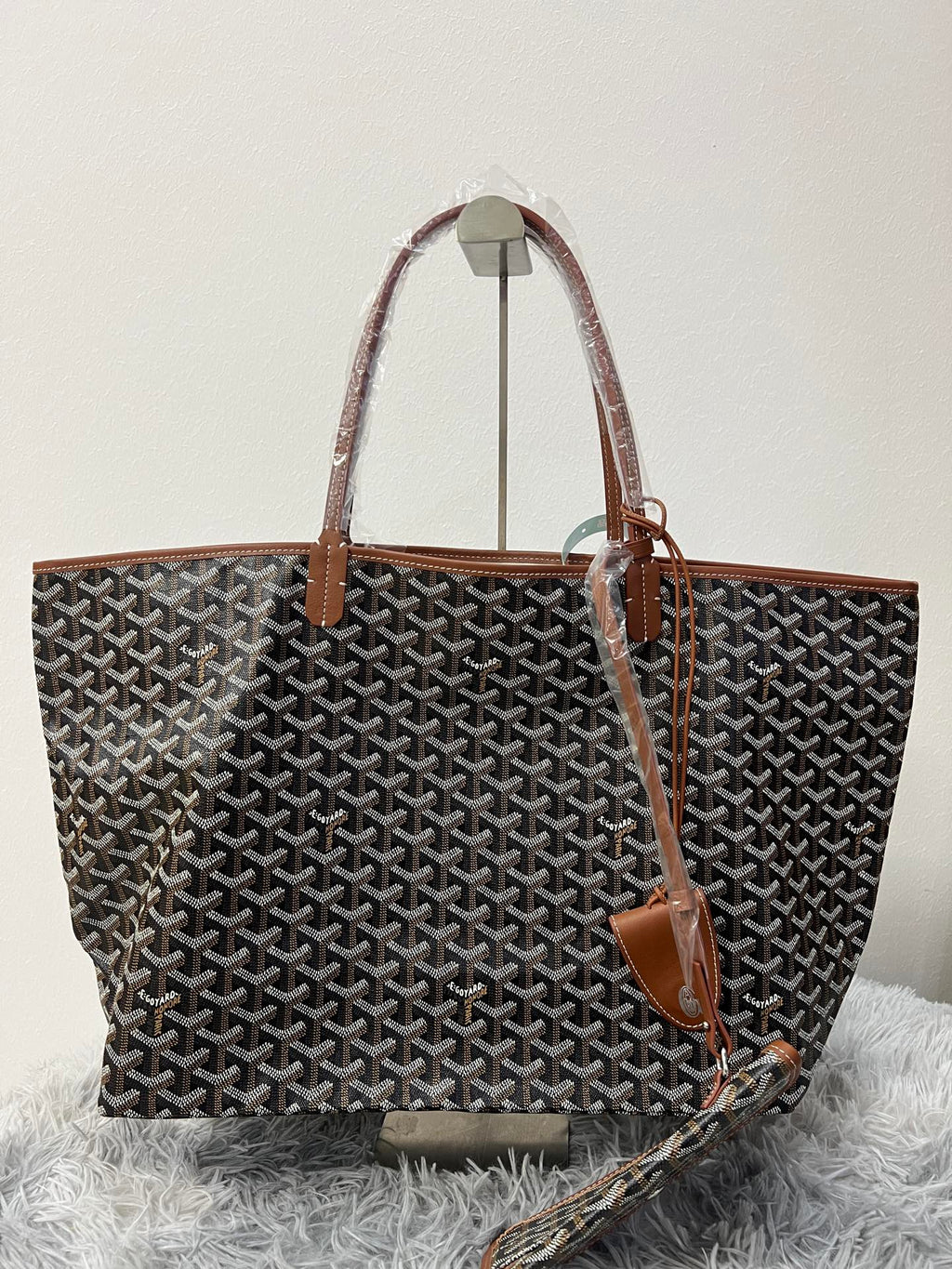Goyard patterned tote bag side view with brown leather handles and hanging tag