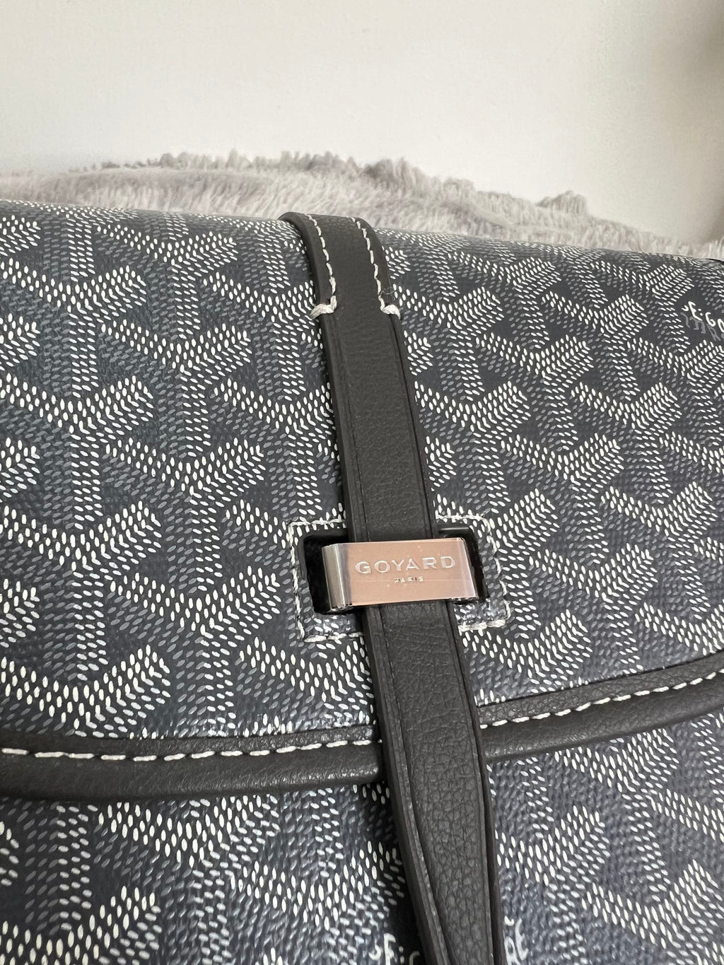 Close-up of crossbody bag flap strap and logo plaque on dark monogram canvas