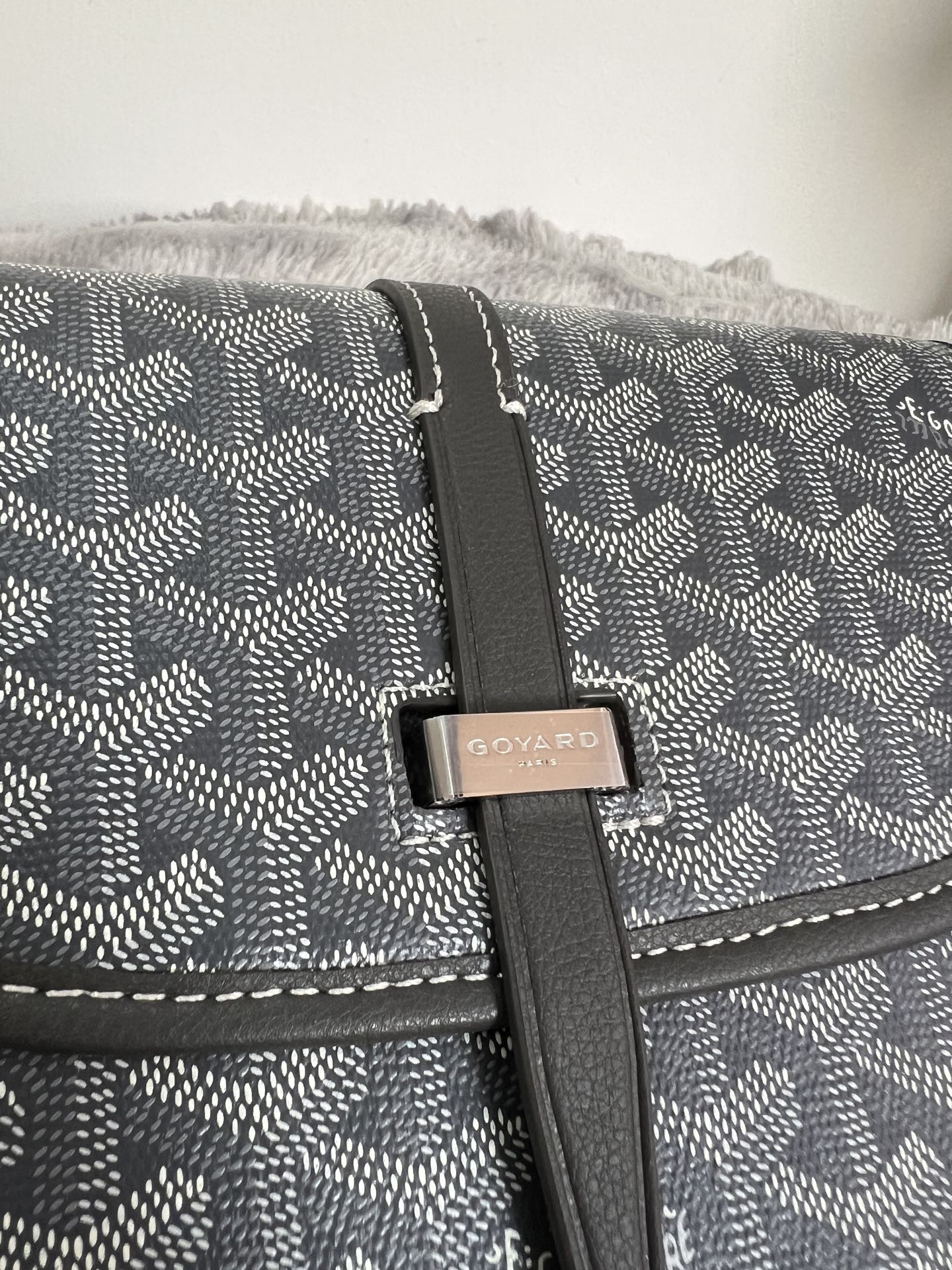 Close-up of crossbody bag flap strap and logo plaque on dark monogram canvas