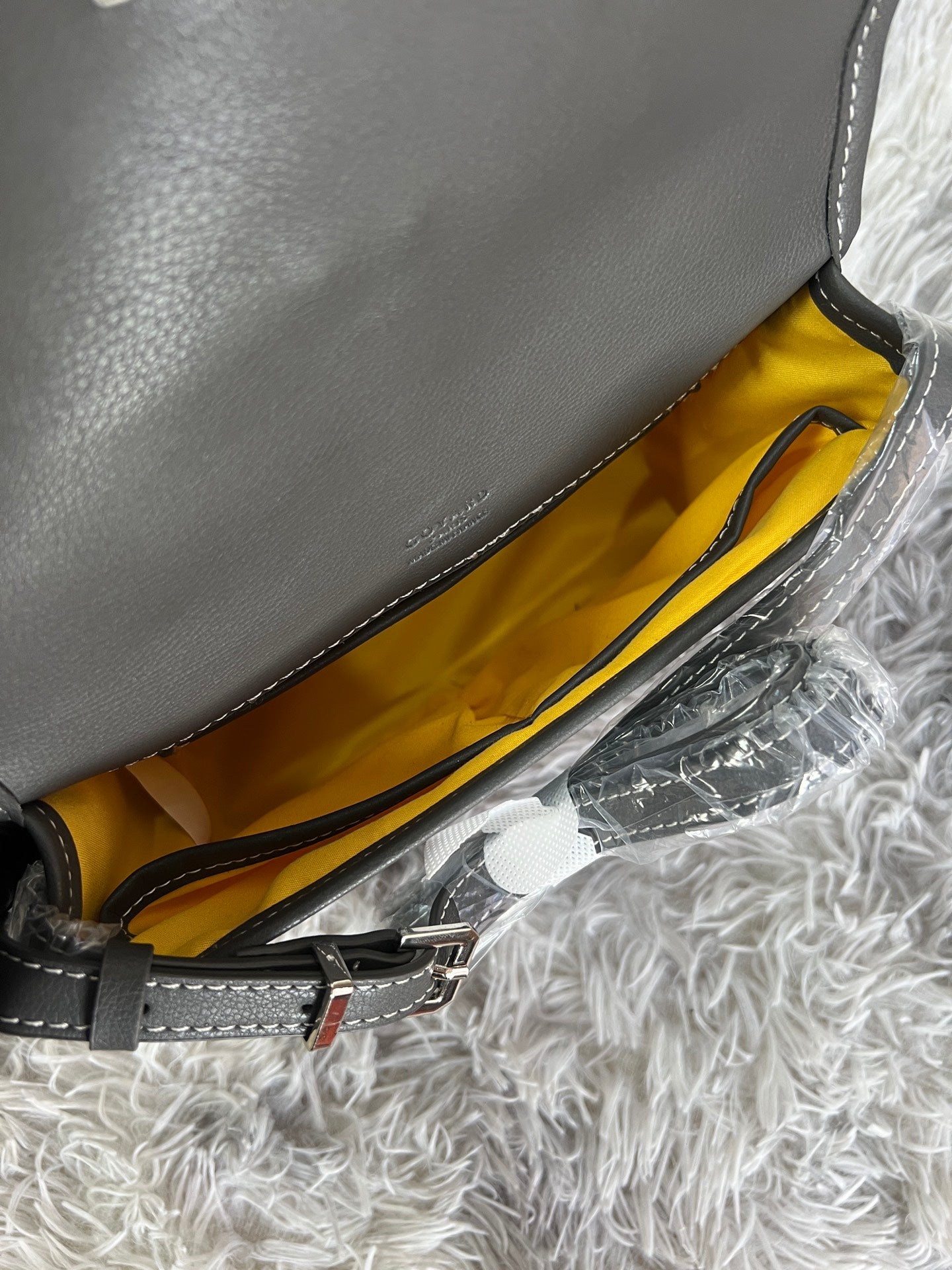 Opened bag with yellow interior lining and black strap, showing inner pocket and stitching