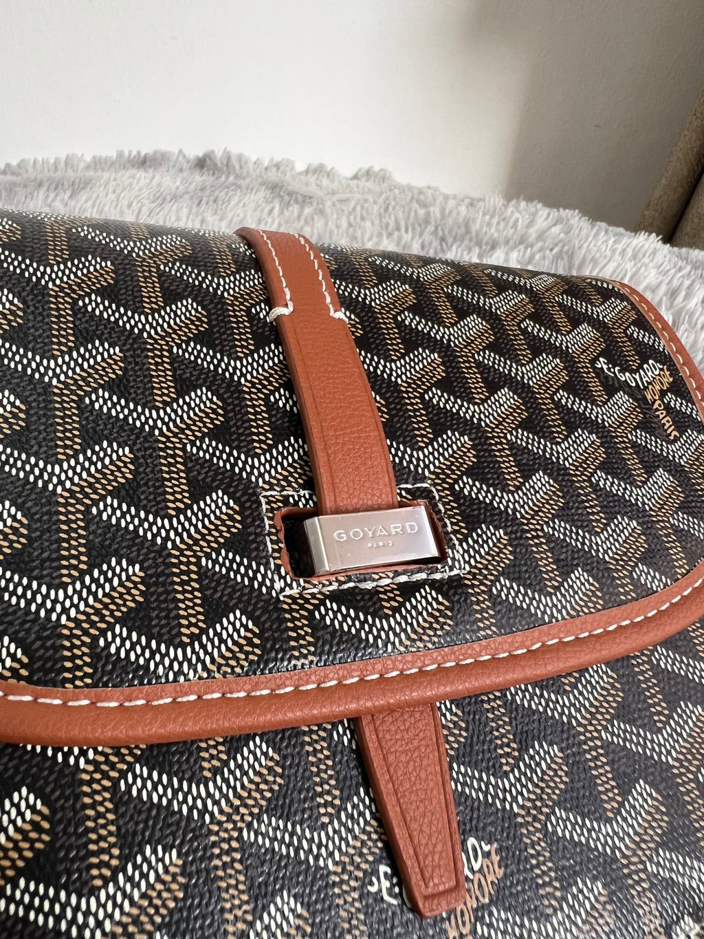 Tan leather strap with metal buckle on dark monogram crossbody bag flap