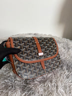 Goyard monogram bag with dark pattern, tan strap, and flap closure, angled view