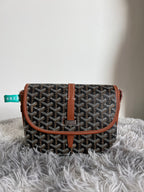 Monogram crossbody bag with dark pattern, tan flap belt strap, and leather trim
