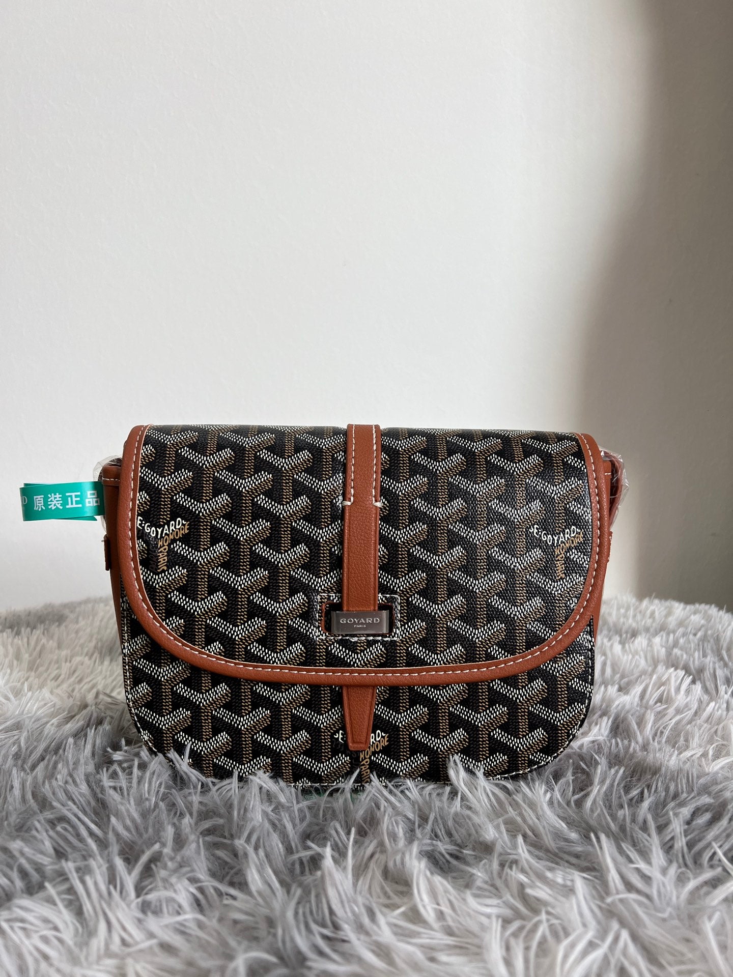 Monogram crossbody bag with dark pattern, tan flap belt strap, and leather trim