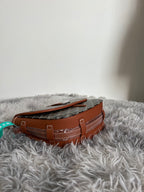 Monogram shoulder bag side view with tan leather handles and stitched seams