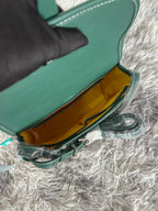 Open green crossbody bag with mustard lining and metal clasp hardware visible