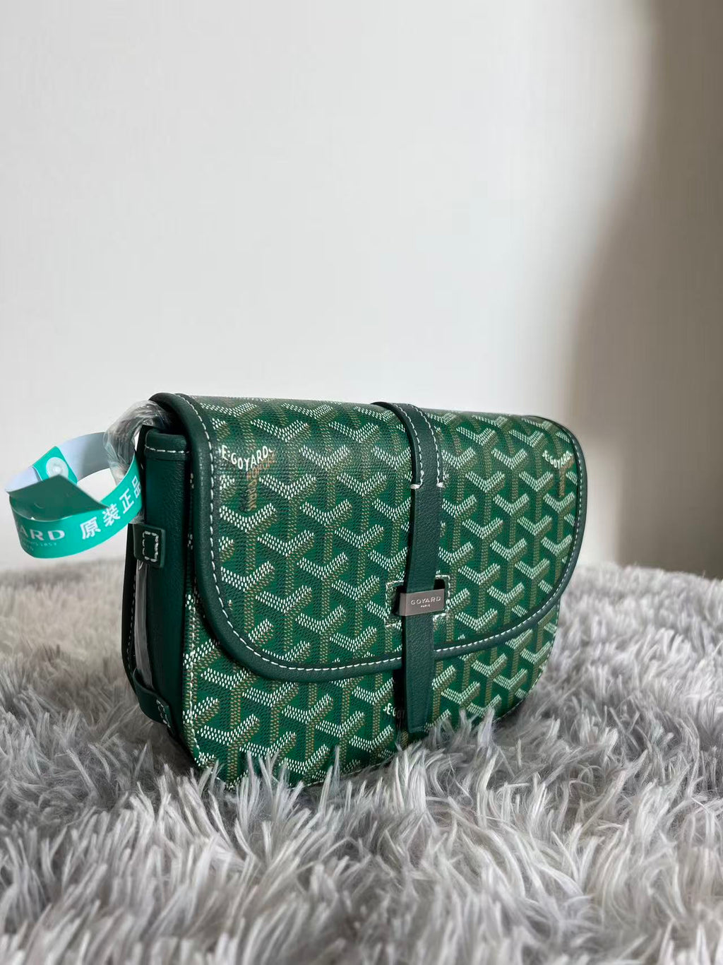 Green patterned Goyard crossbody bag with leather strap and hanging brand tag