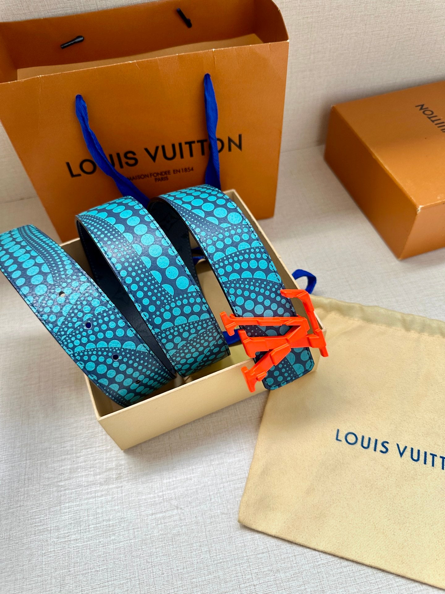 Blue-and-turquoise patterned belt with red LV buckle, shown folded in the box.