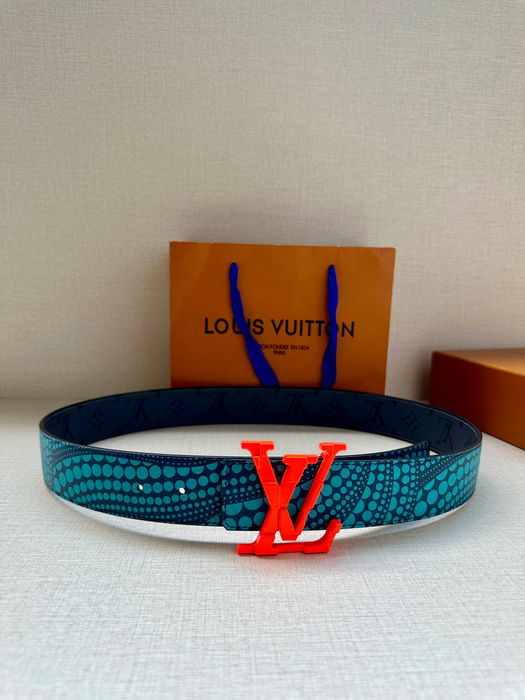 Blue patterned belt with red LV buckle, dark leather strap with embossed monogram.