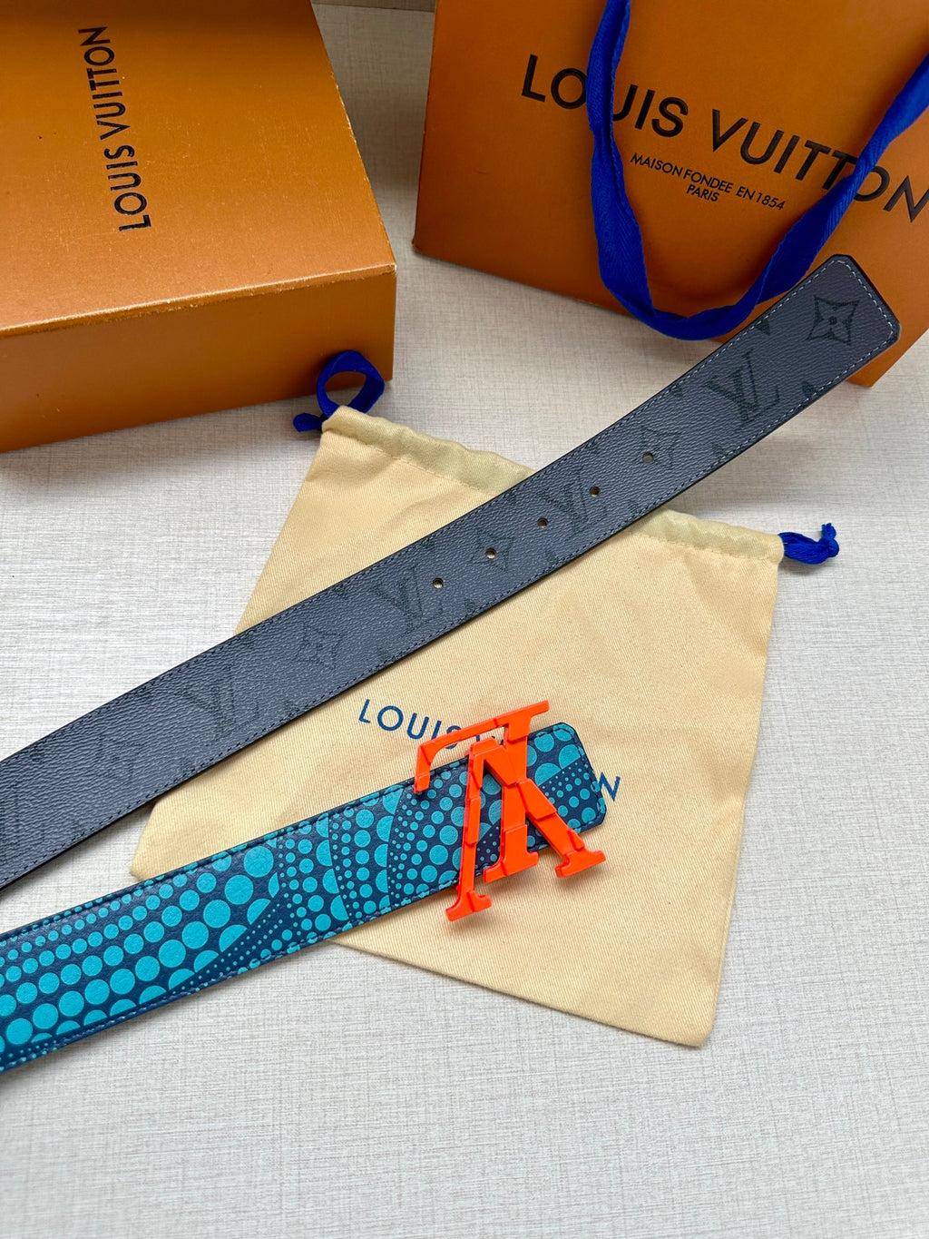 Blue monogram-pattern belt with red LV buckle, long strap laid across a pouch.