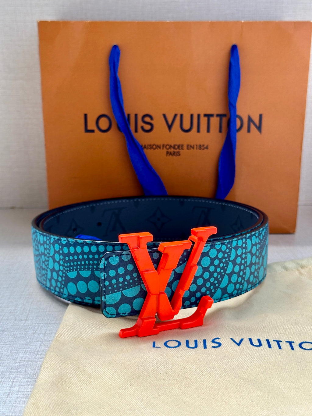 Turquoise-and-blue patterned belt with bold red LV buckle, centered on the strap.