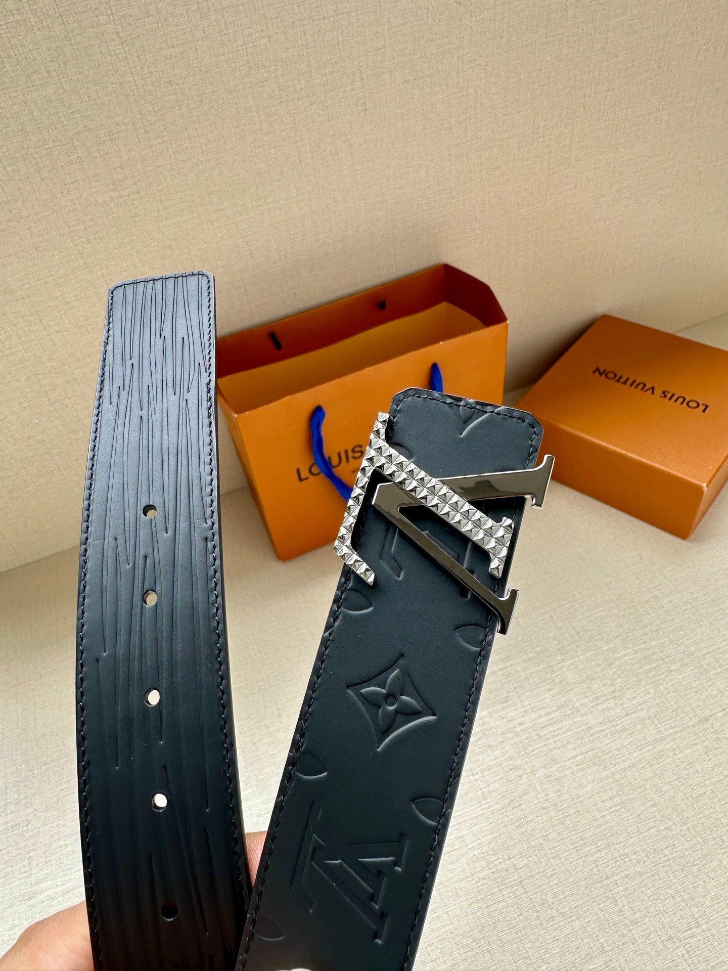 Navy Louis Vuitton embossed belt with silver-tone LV buckle, laid flat for view.