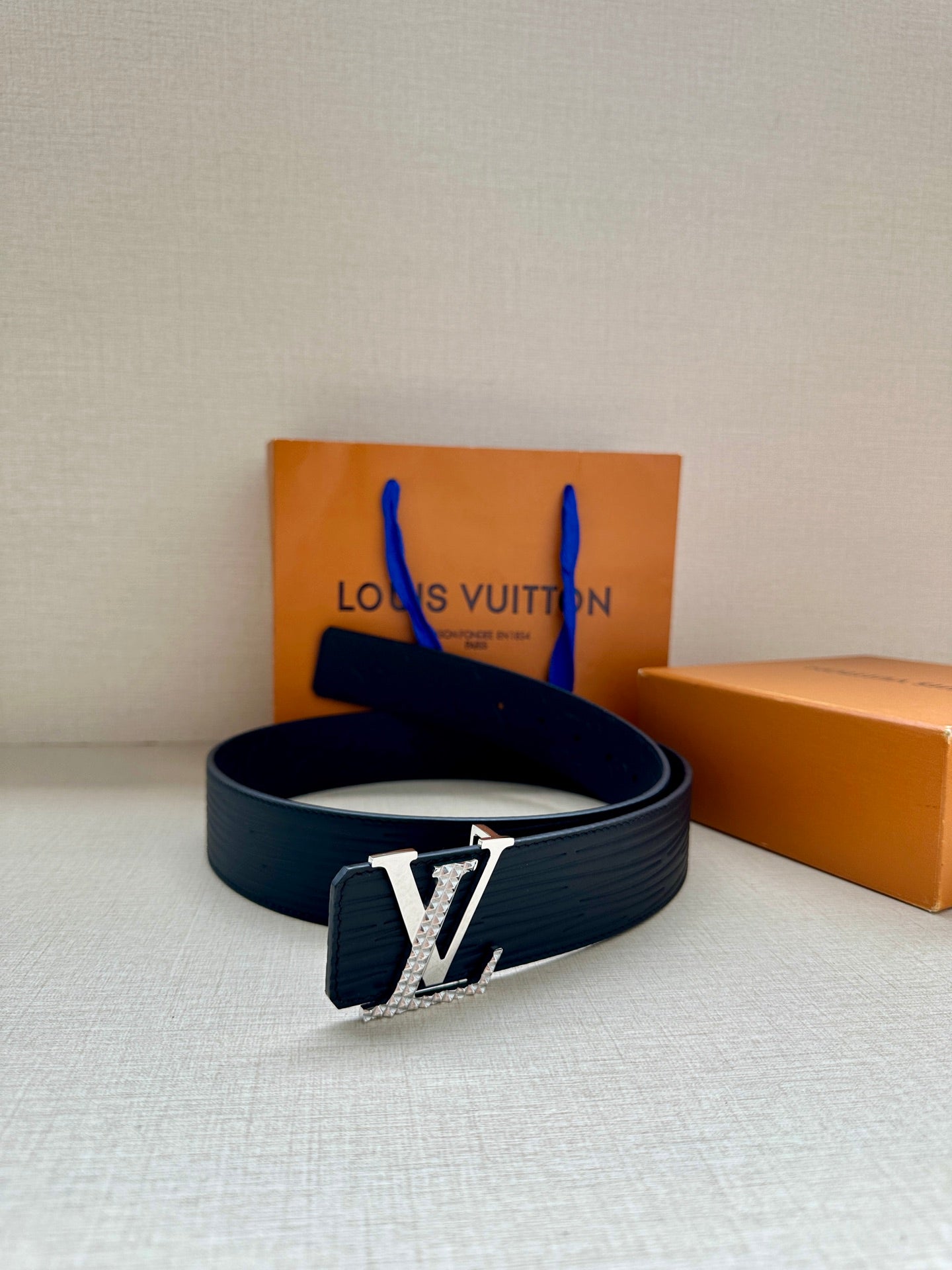 Navy Louis Vuitton leather belt with silver-tone LV buckle, shown with strap looped.