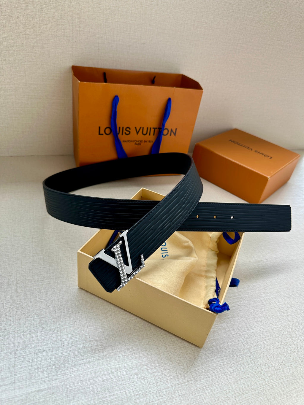 Navy Louis Vuitton belt with silver-tone LV buckle and textured strap, laid on tray.