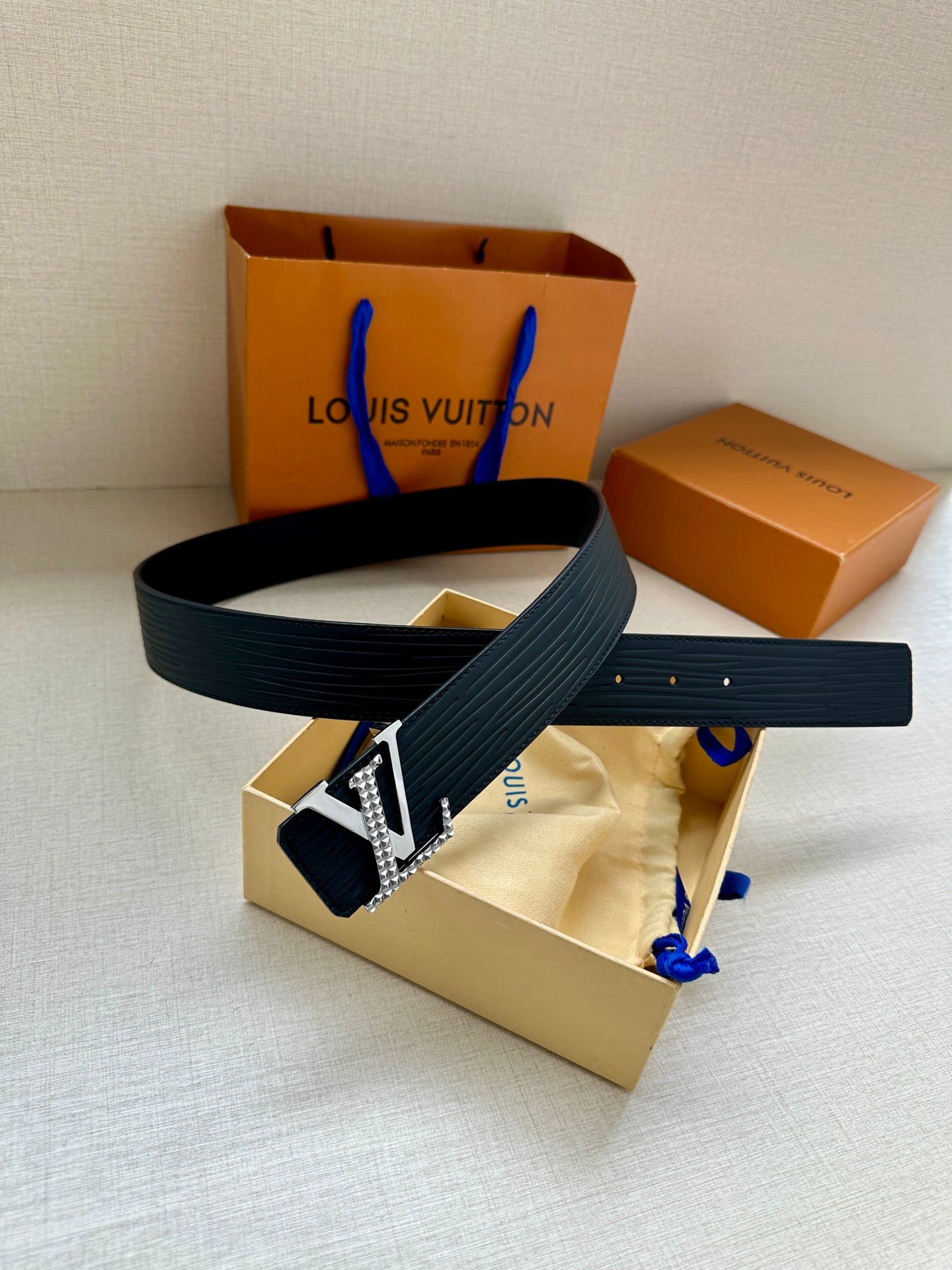 Navy Louis Vuitton belt with silver-tone LV buckle and textured strap, laid on tray.