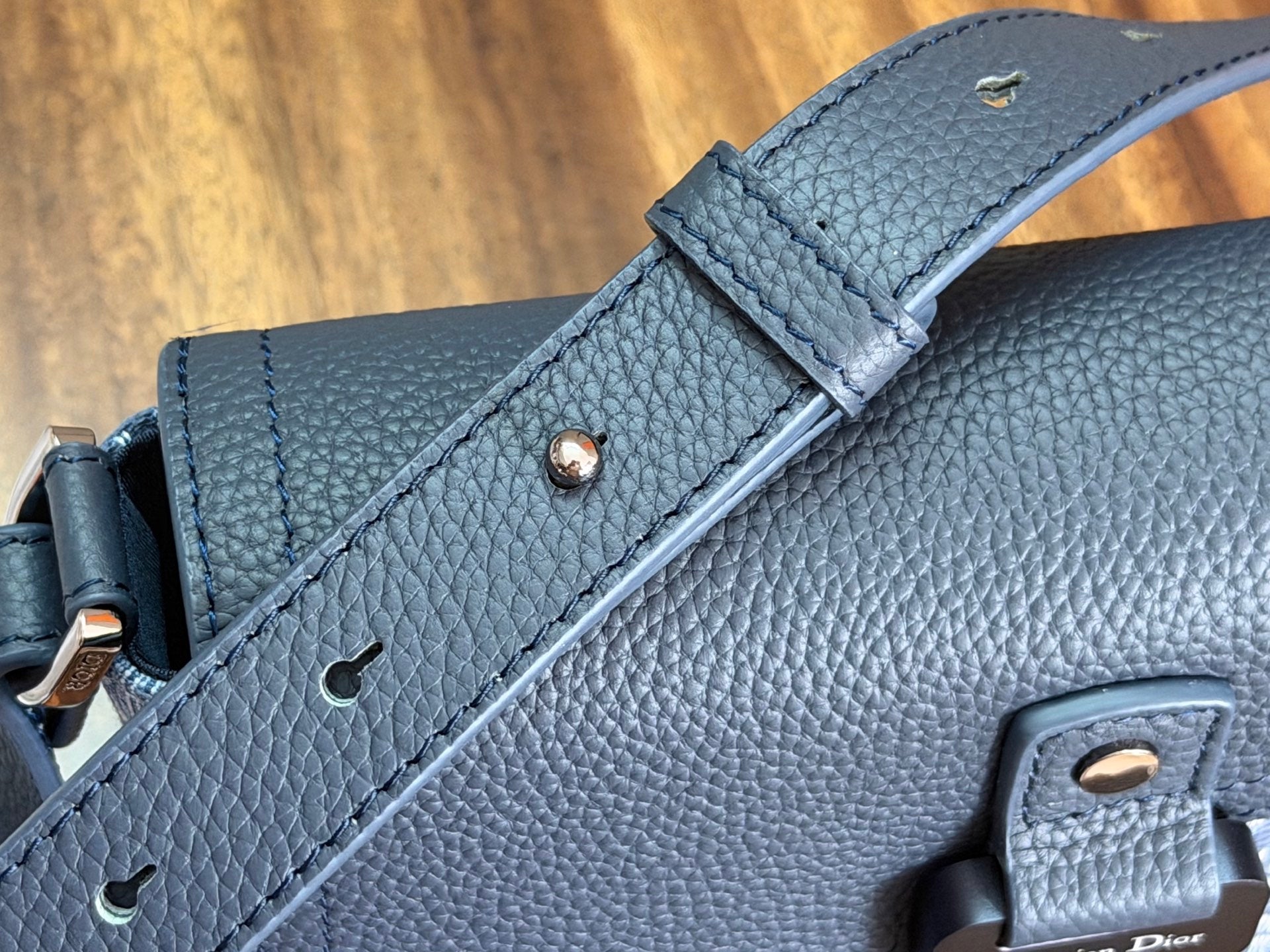 Blue leather crossbody bag with stitched strap, gold snap details, and Dior emblem
