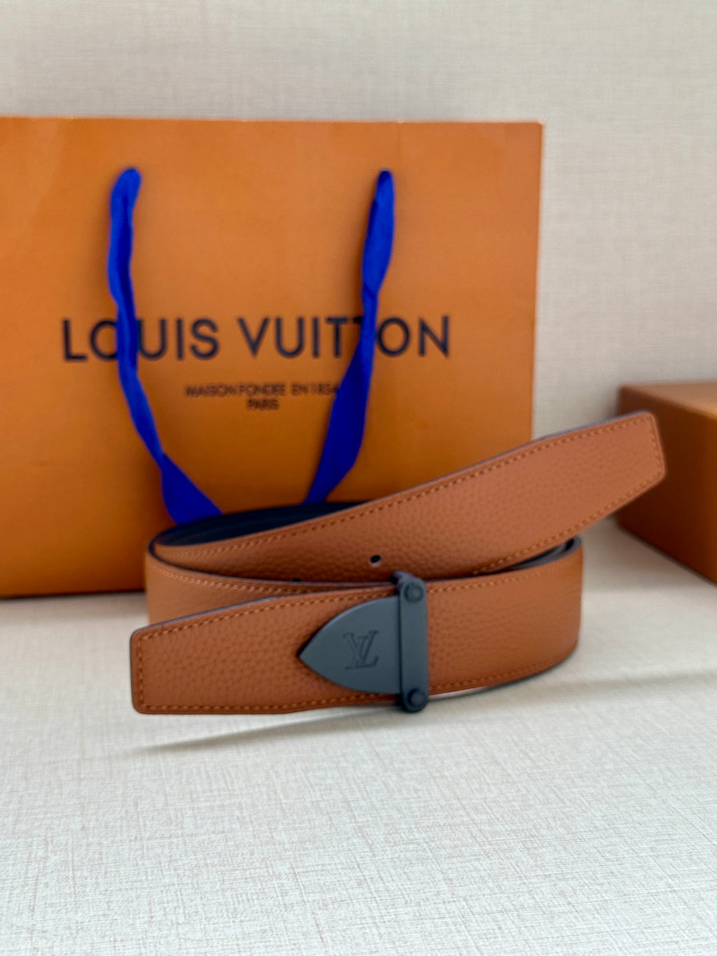 Tan leather belt with dark blue buckle plate and stitched strap edge