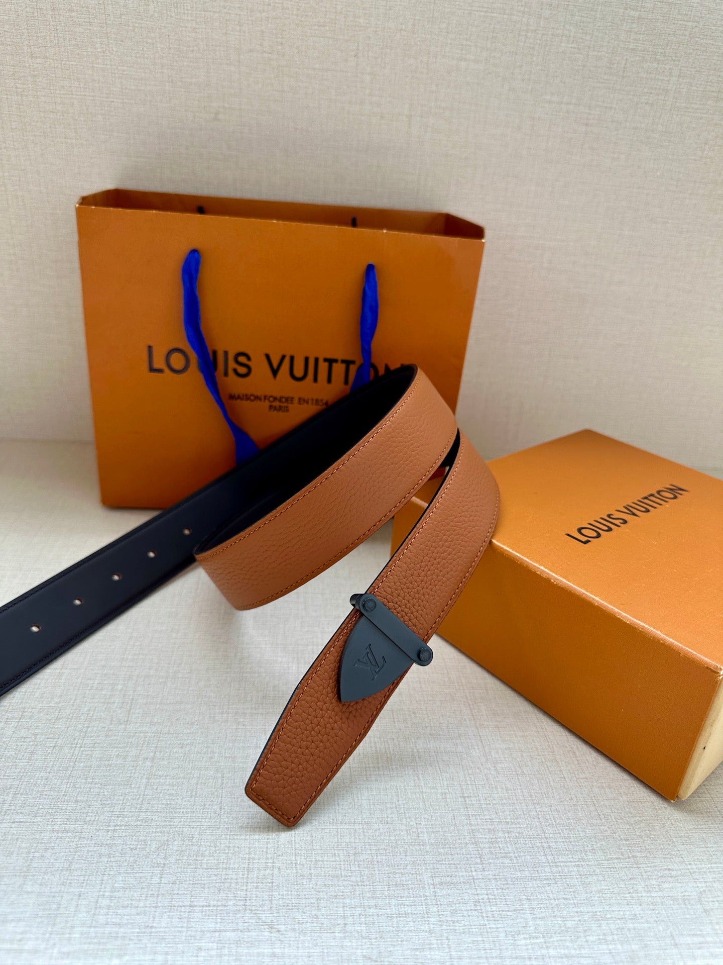 Tan leather belt with dark blue buckle, straps draped for display