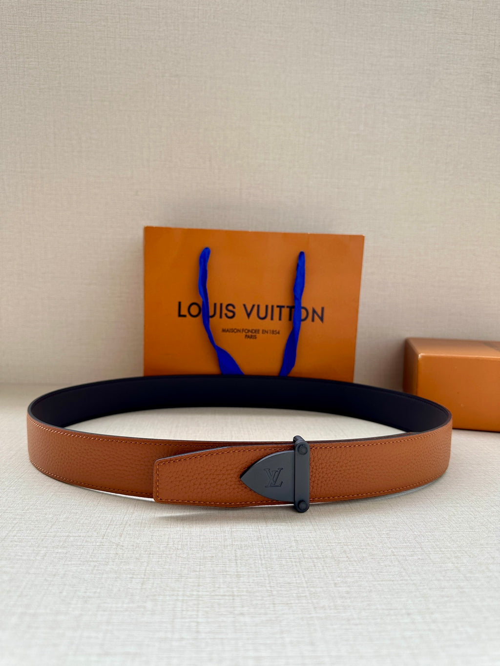 Tan leather belt with dark blue buckle and keeper tab