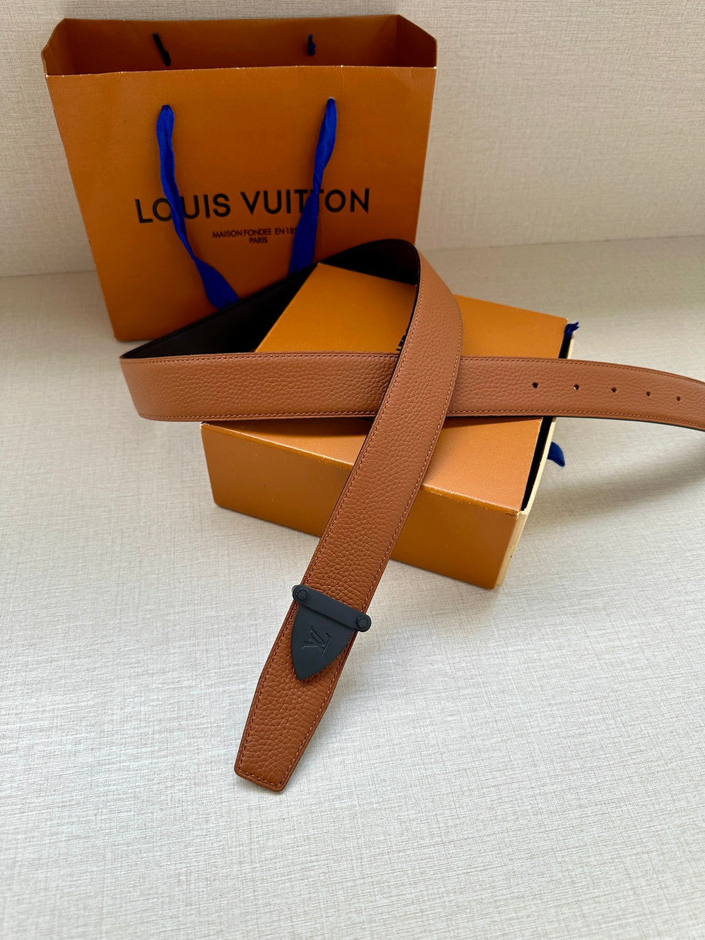 Tan leather belt with dark blue buckle, long strap tail visible