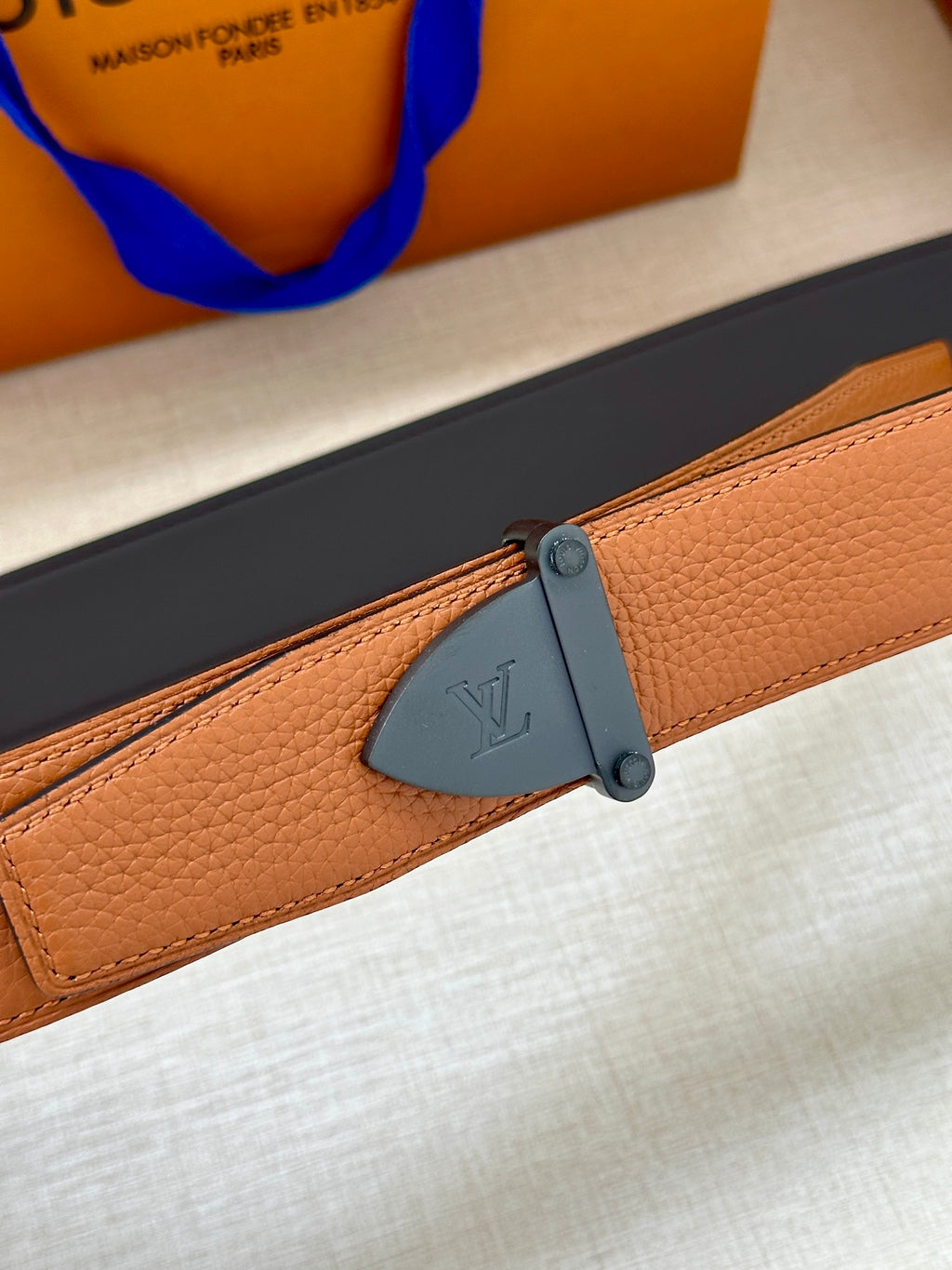 Tan leather belt close-up with dark blue clasp and embossed buckle plate