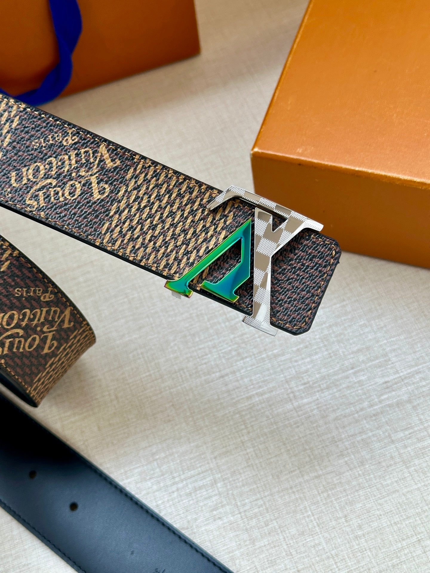 Louis Vuitton belt buckle close-up with teal inlay on silver clasp and dark monogram strap