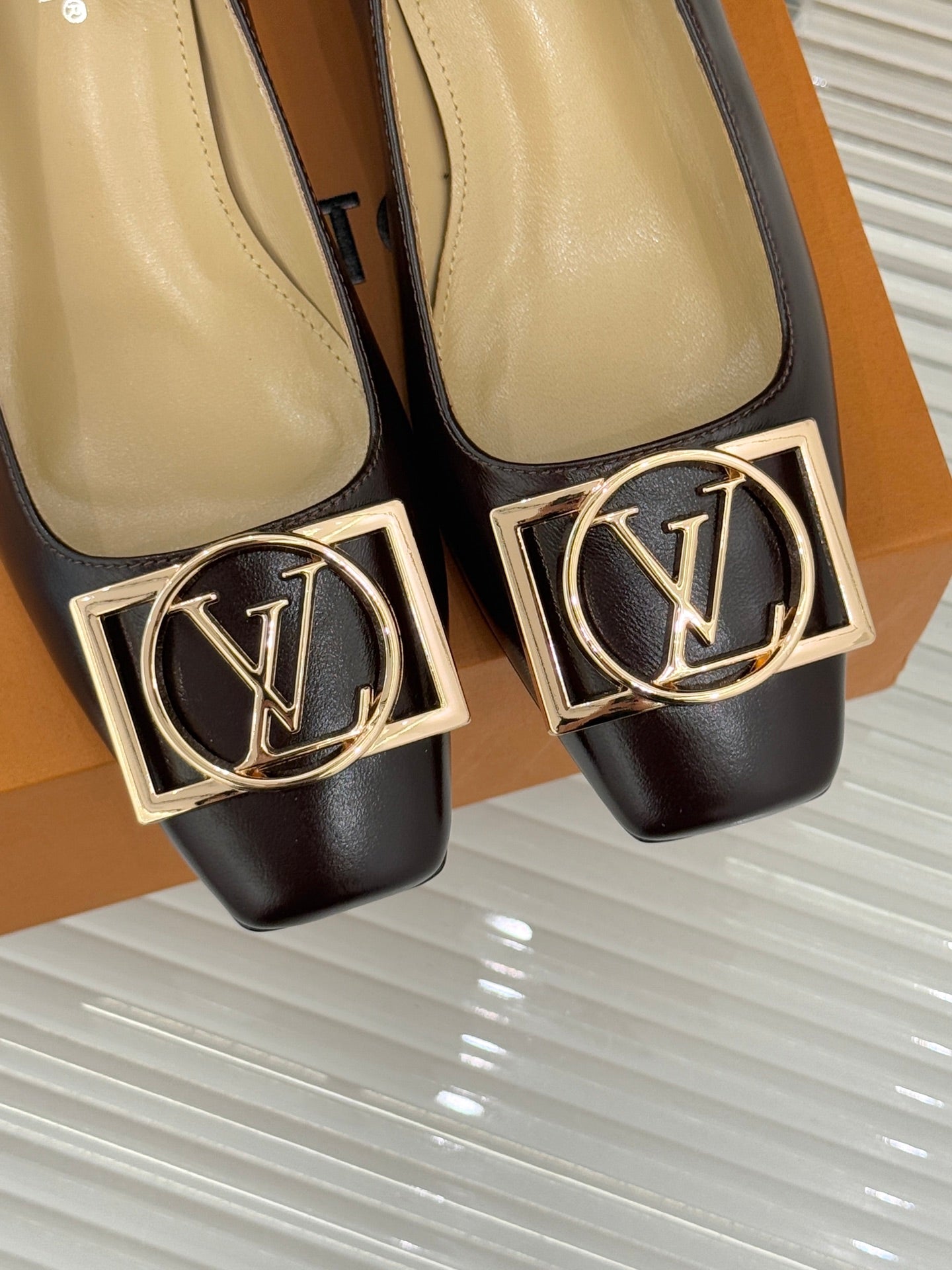 Close-up of women's dark brown square-toe pumps with gold LV logo ornament and trim