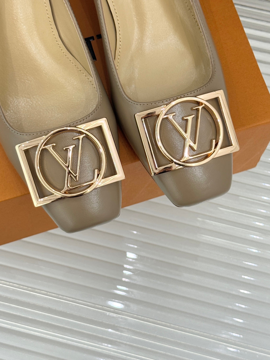 Close-up of beige Louis Vuitton ladies pumps with gold LV logo square buckle