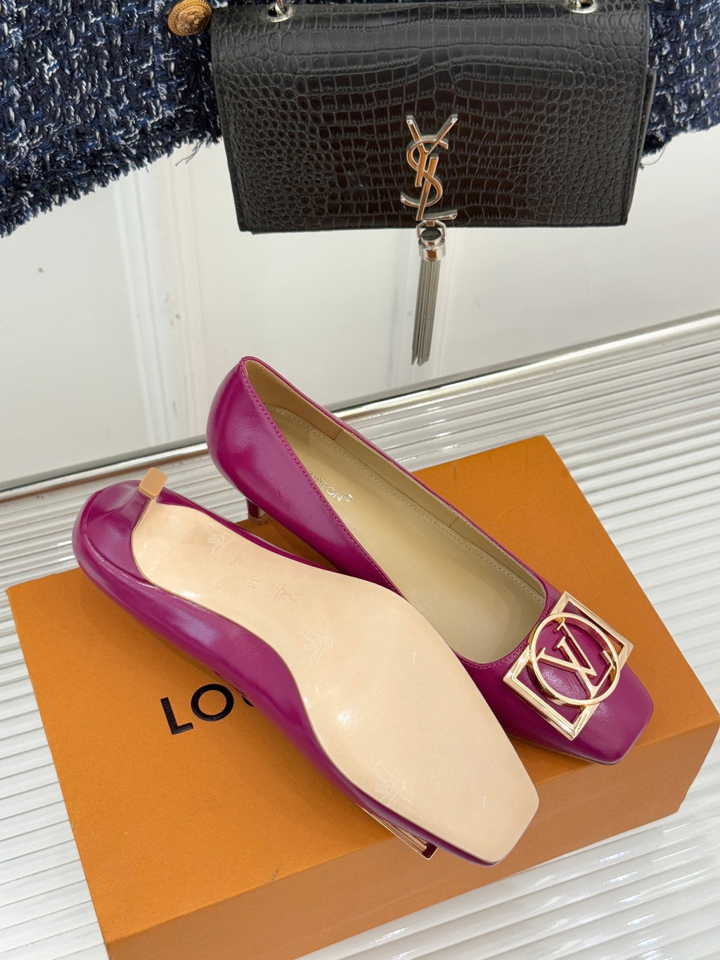 Pink Louis Vuitton heels with gold LV logo buckle detail, laid on orange box