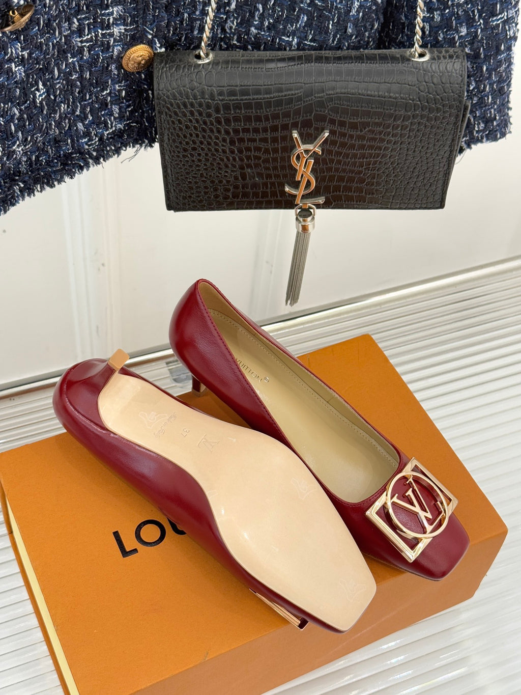 Louis Vuitton ladies red pumps with gold LV buckle, pair on orange box beside black bag