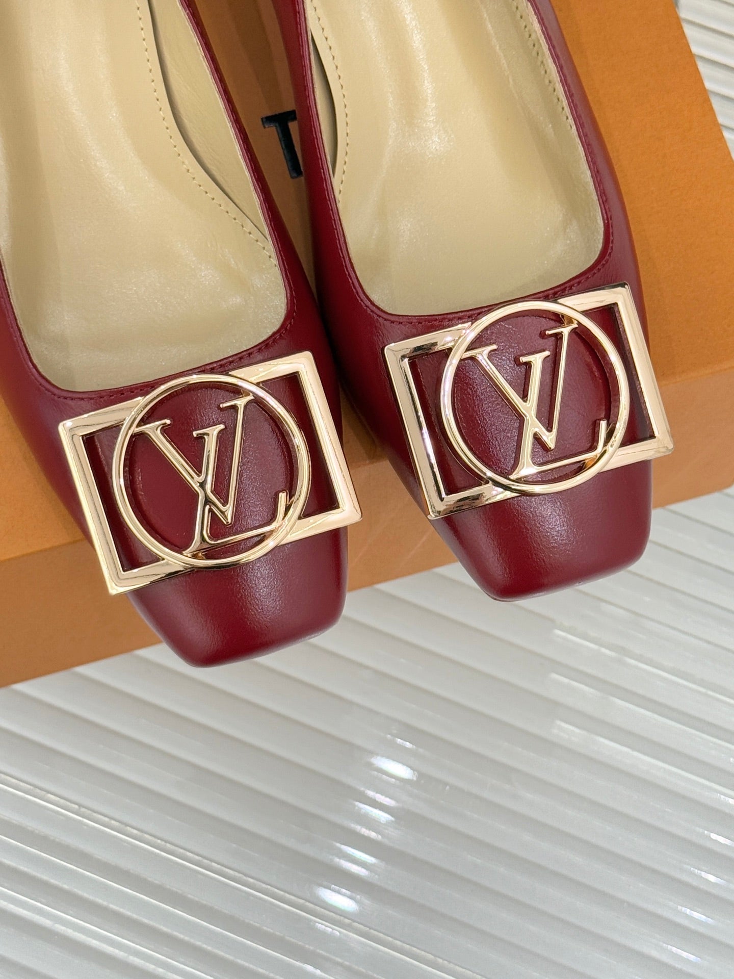 Louis Vuitton ladies red pumps close-up, gold LV buckle at toes, beige insoles