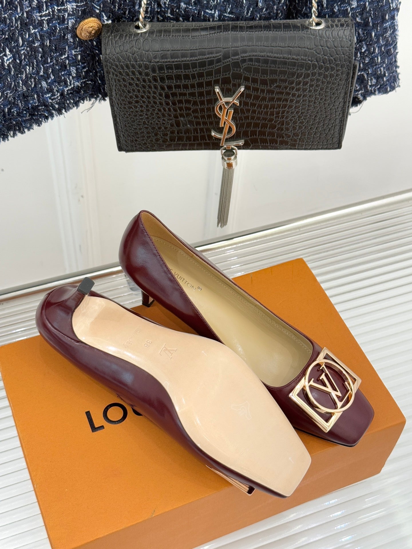 Burgundy low-heel pumps with gold square logo buckle detail and cream insole.