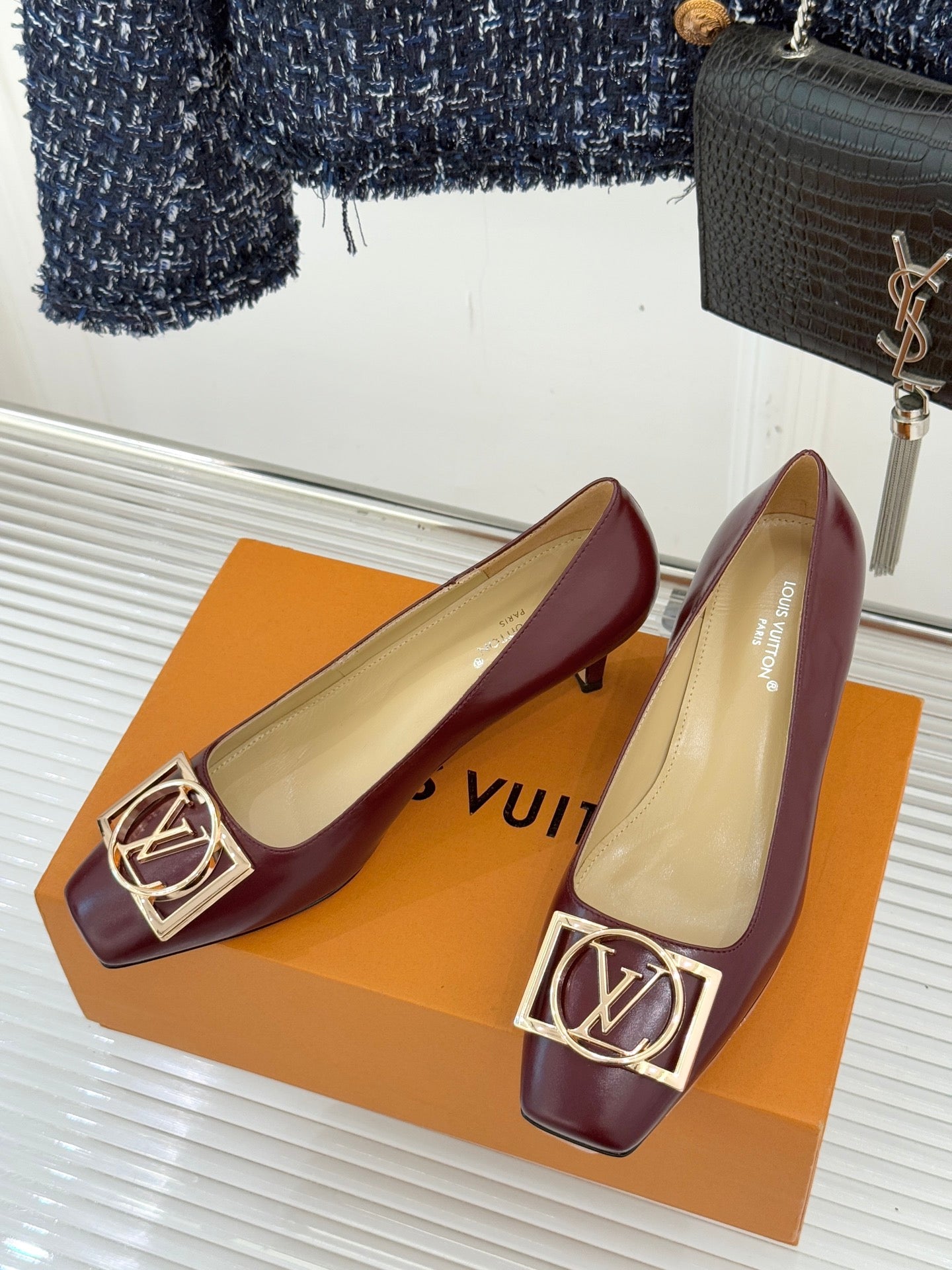 Pair of burgundy low-heel pumps with gold square logo buckle on the toe.