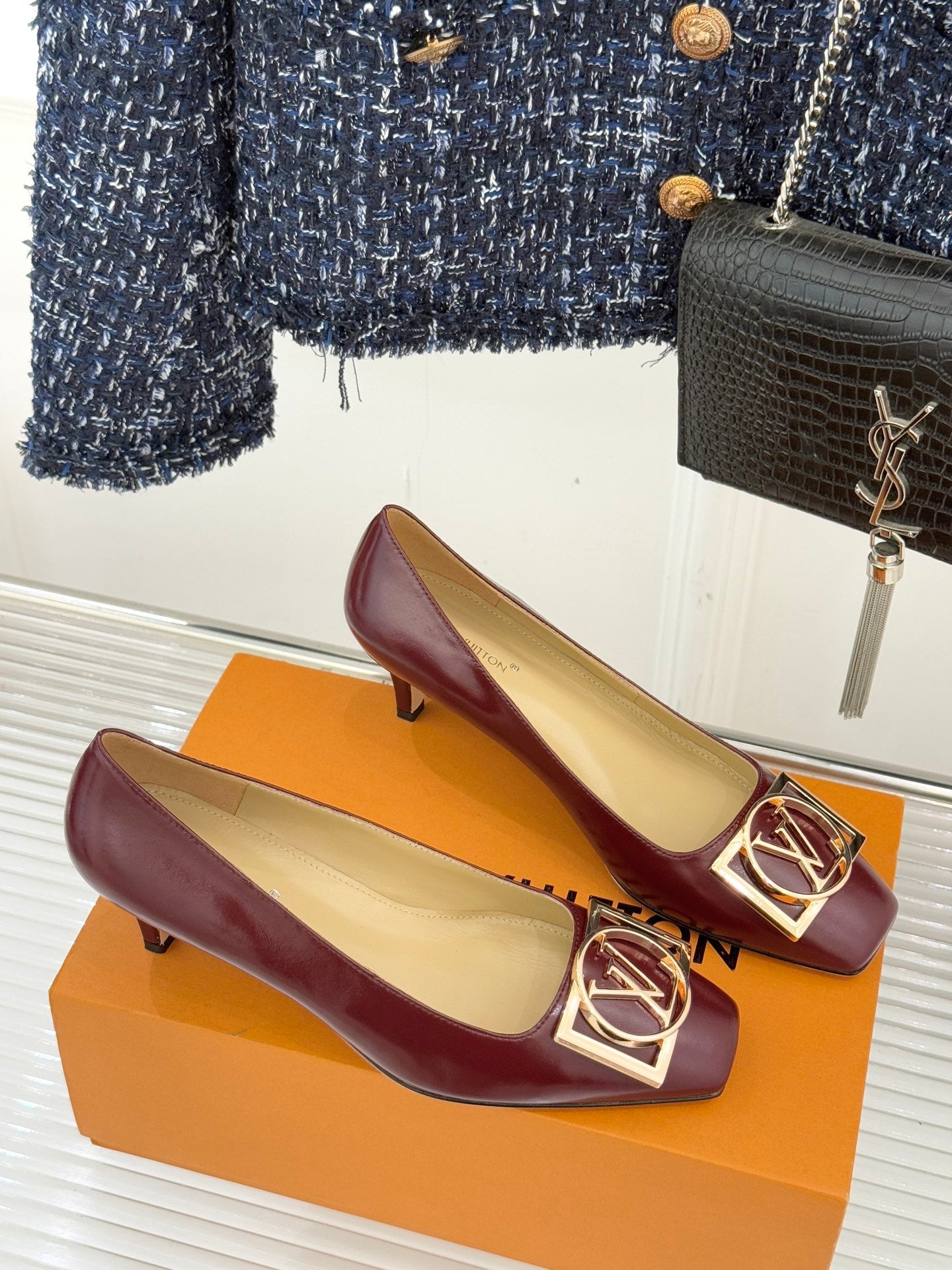 Burgundy low-heel pumps with gold square logo buckles and cream insoles visible.