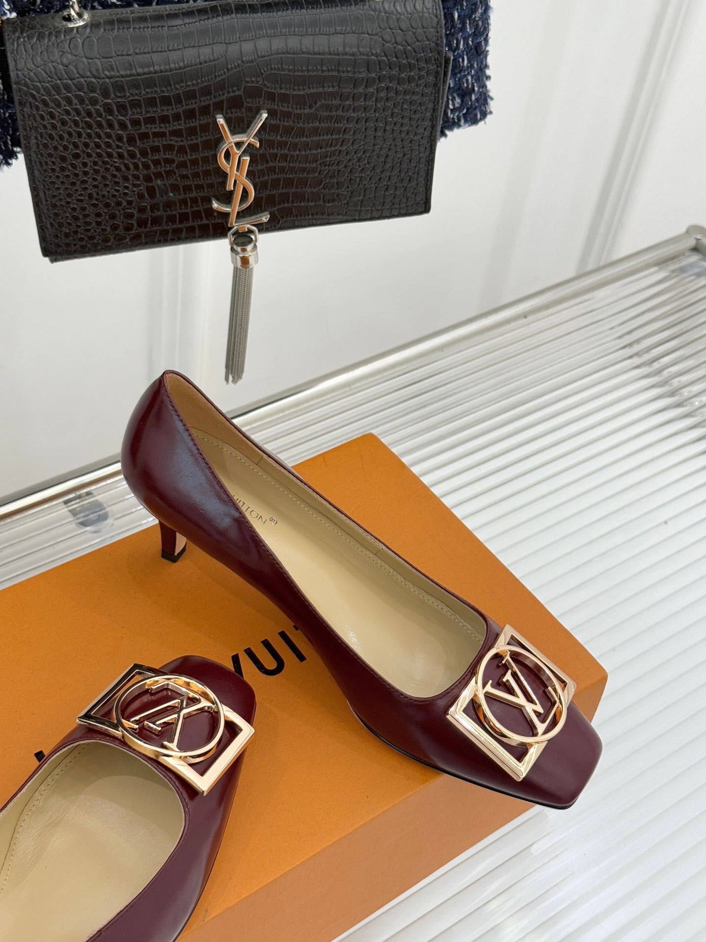 Burgundy leather low-heel pumps with gold square logo buckle, cream lining.